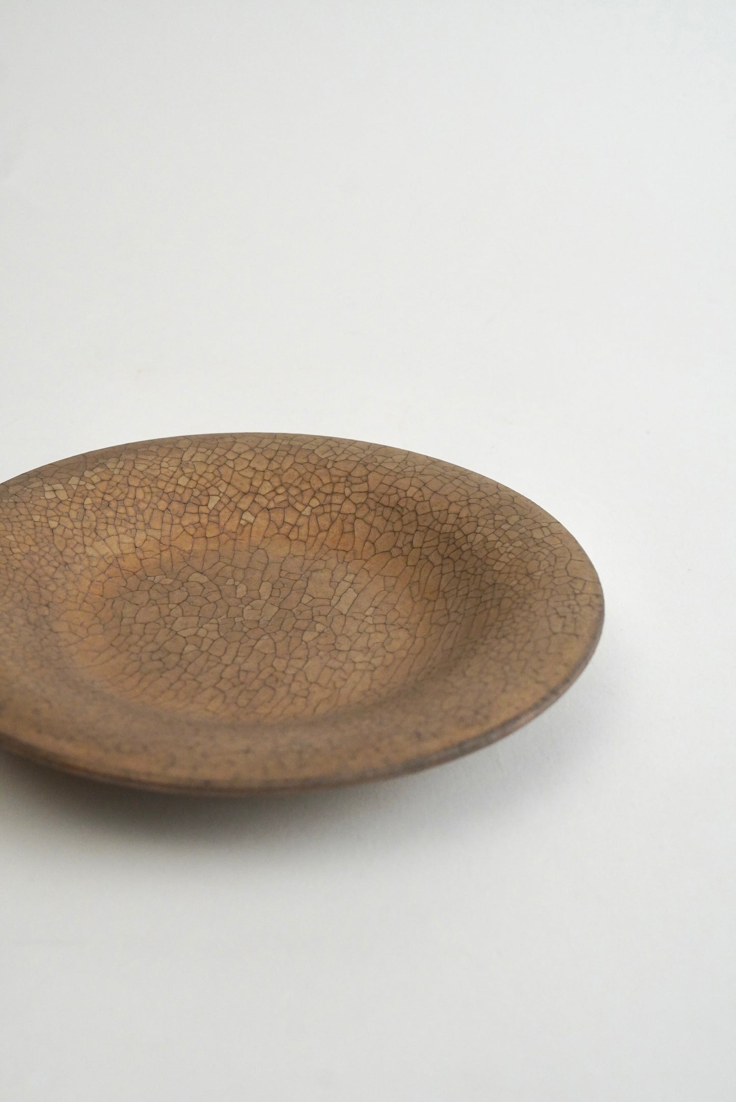 A shallow round ceramic plate with a brown earthy glaze and a prominent crackle pattern, photographed on a clean white background.