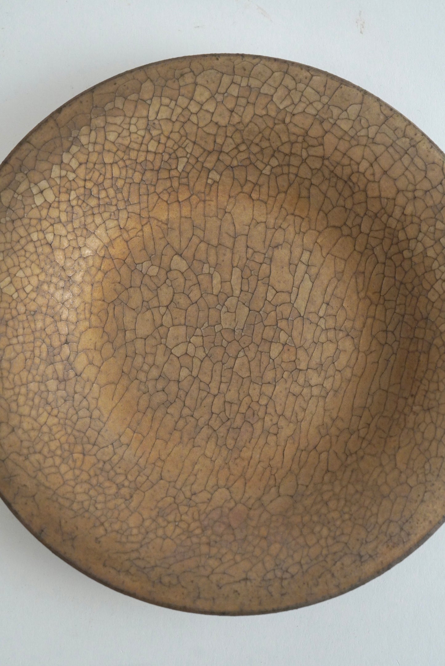 A round ceramic plate with a brown and beige crackle glaze pattern, photographed from directly above on a plain white background.