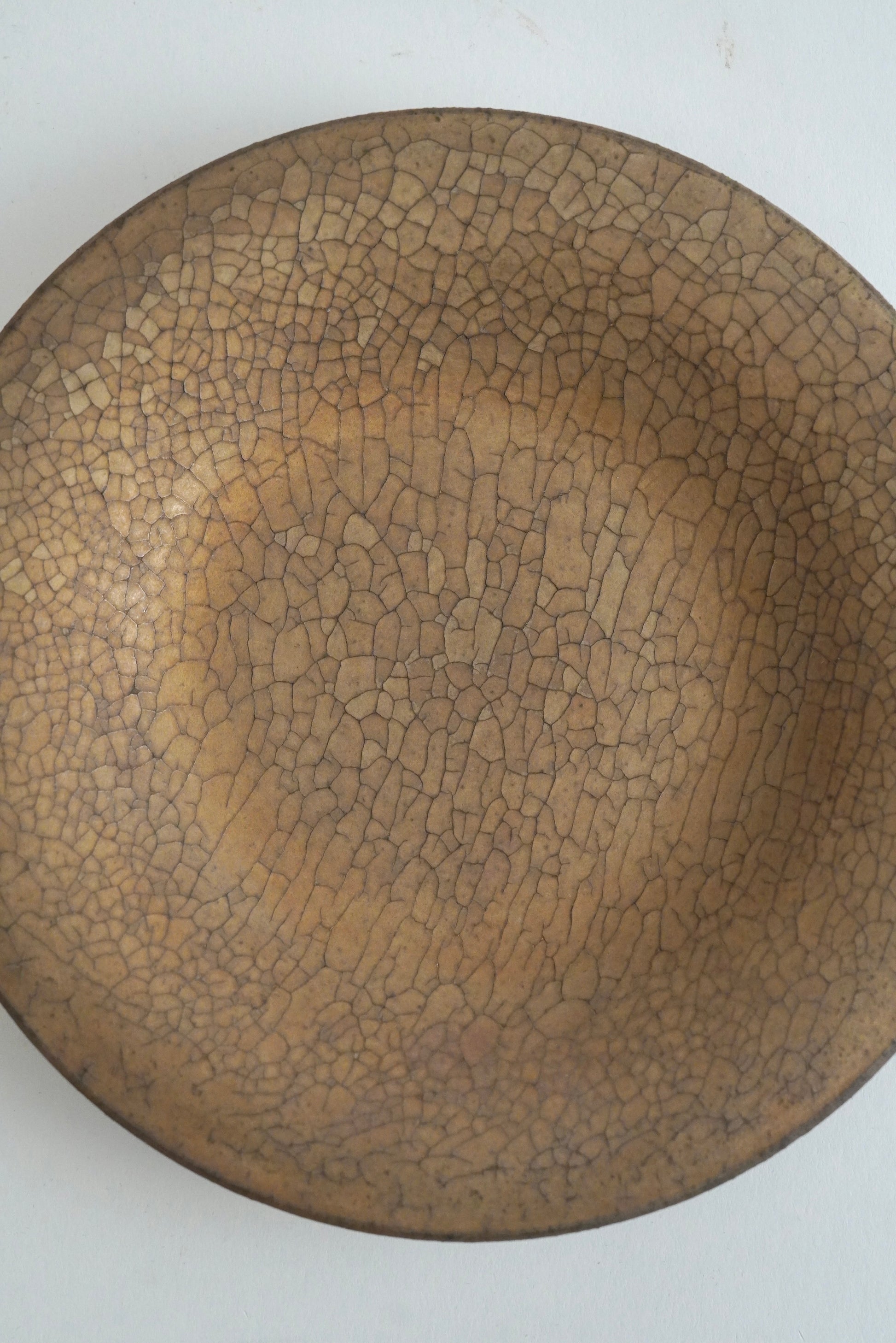 A round ceramic plate with a brown and beige crackle glaze pattern, photographed from directly above on a plain white background.