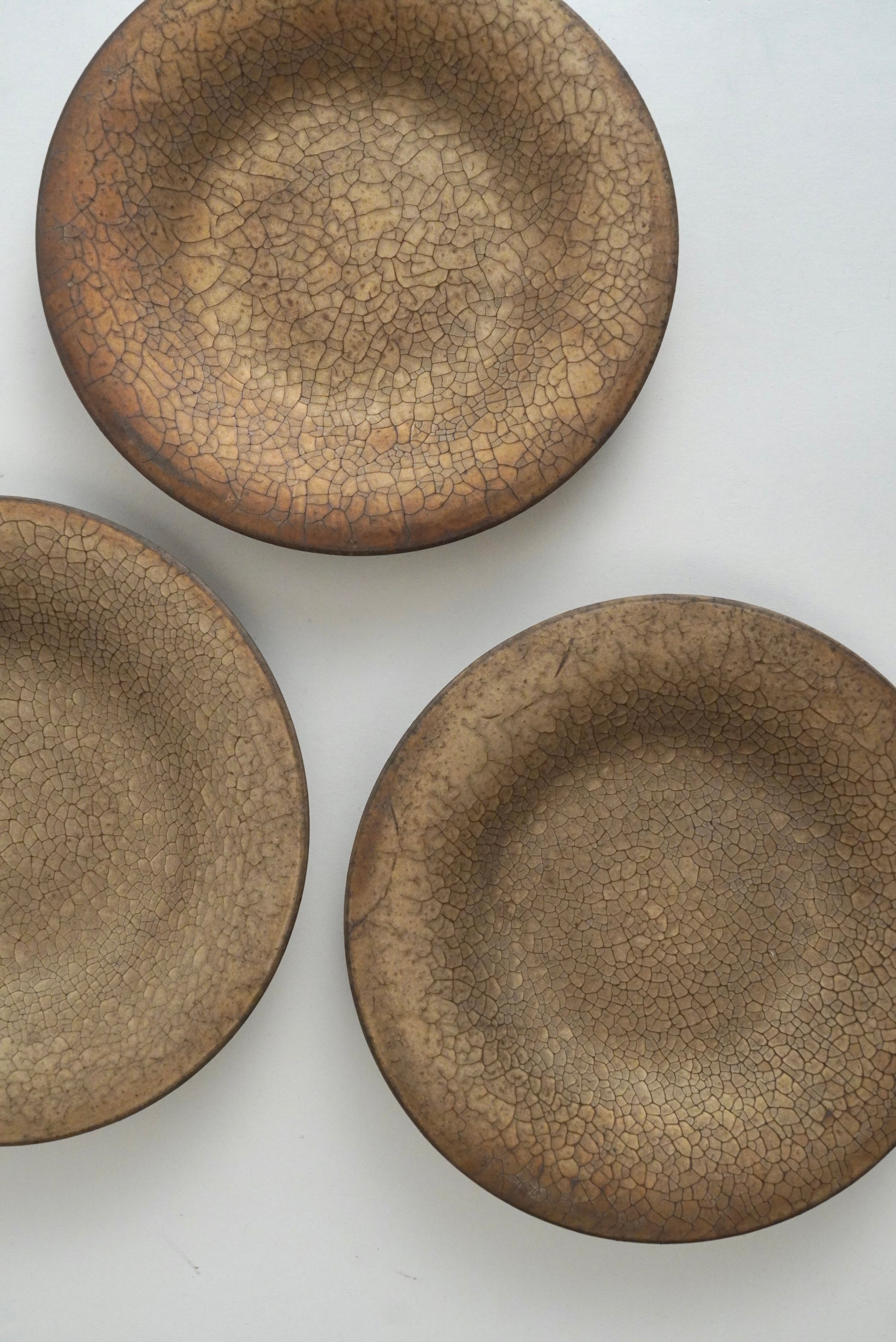 Three shallow round ceramic dishes with a brown and beige crackle glaze, arranged on a plain white background.