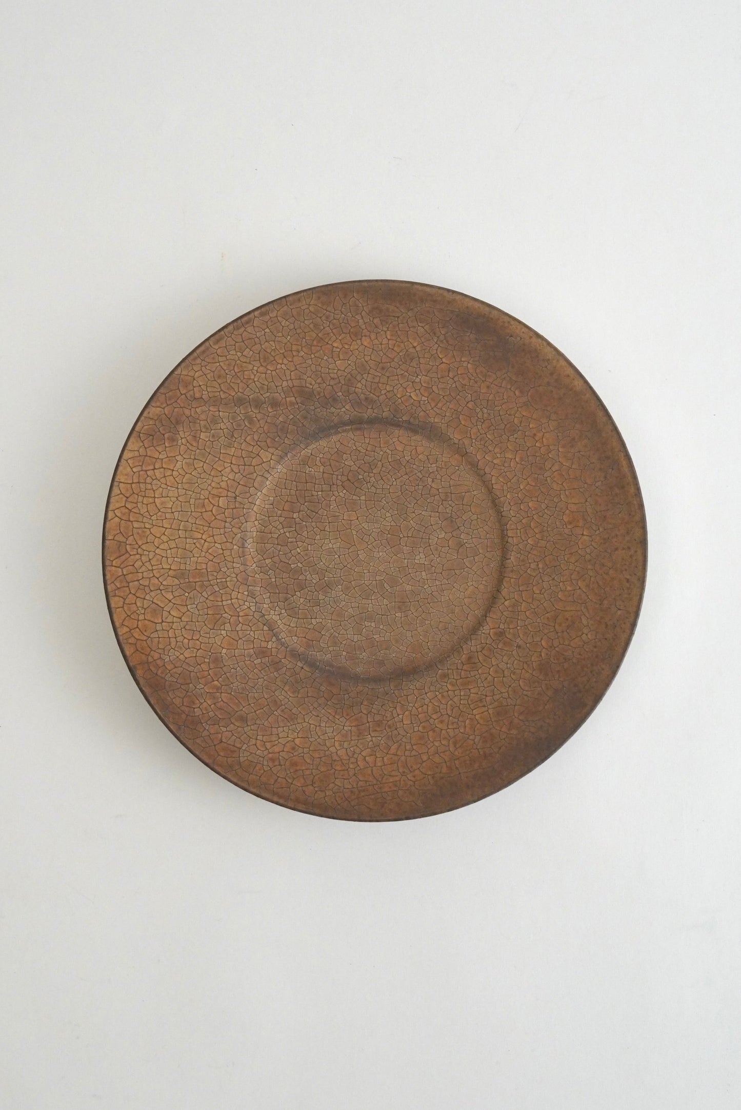 A round ceramic plate with a textured, rustic brown glaze, photographed from directly above on a clean white background.
