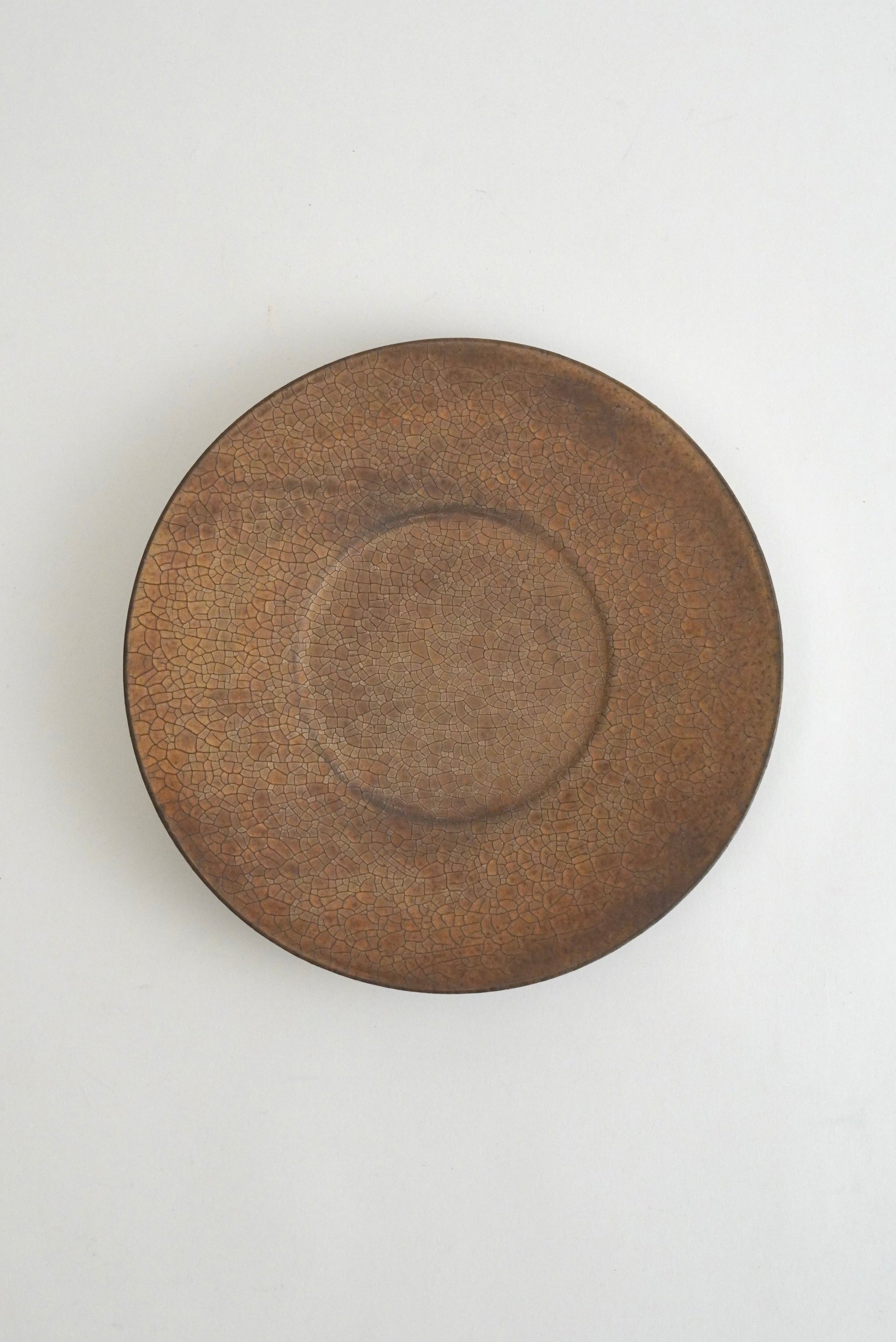 A round ceramic plate with a textured, rustic brown glaze, photographed from directly above on a clean white background.