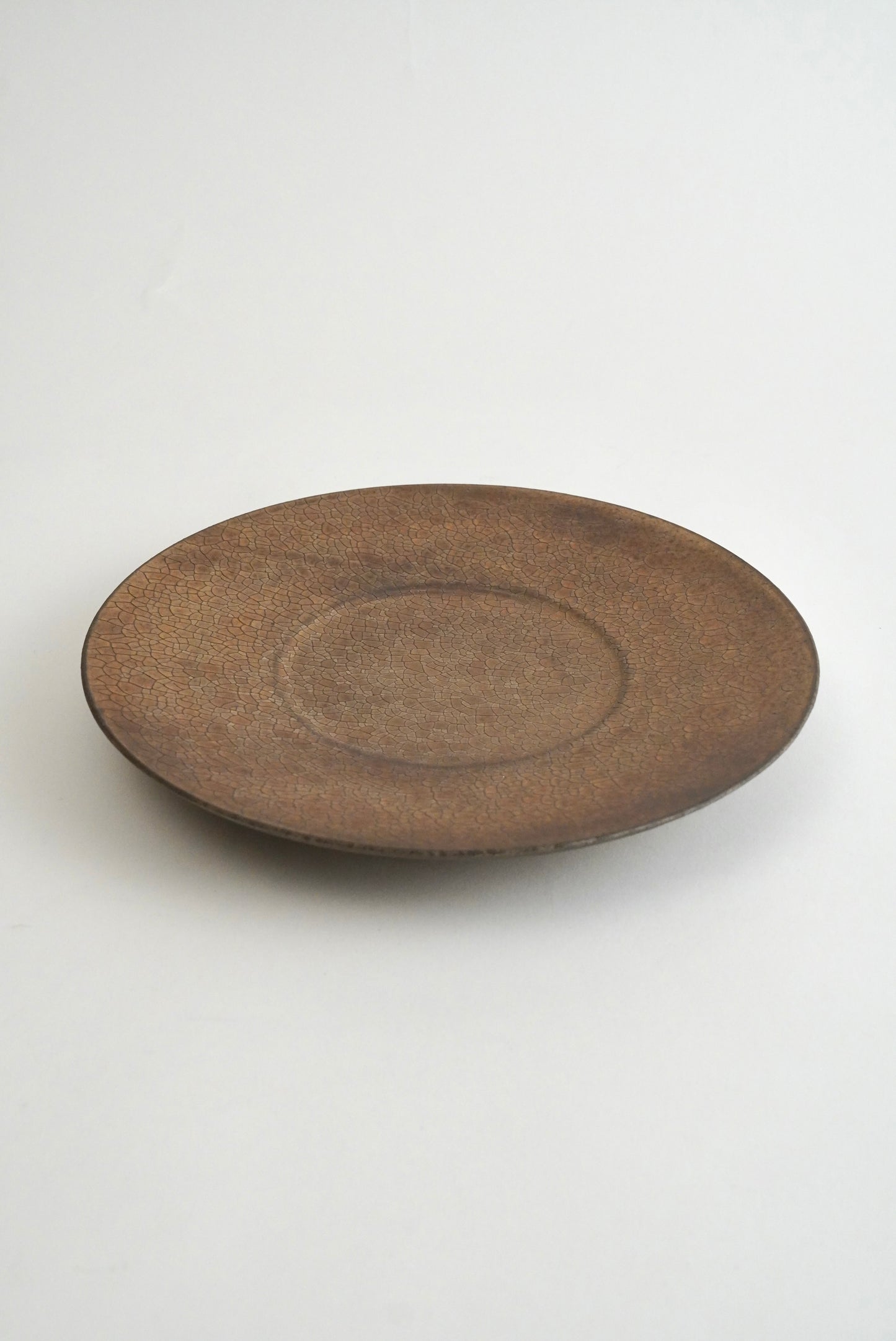 A round, shallow ceramic plate or tray with a textured, matte brown glaze, photographed against a clean white background.