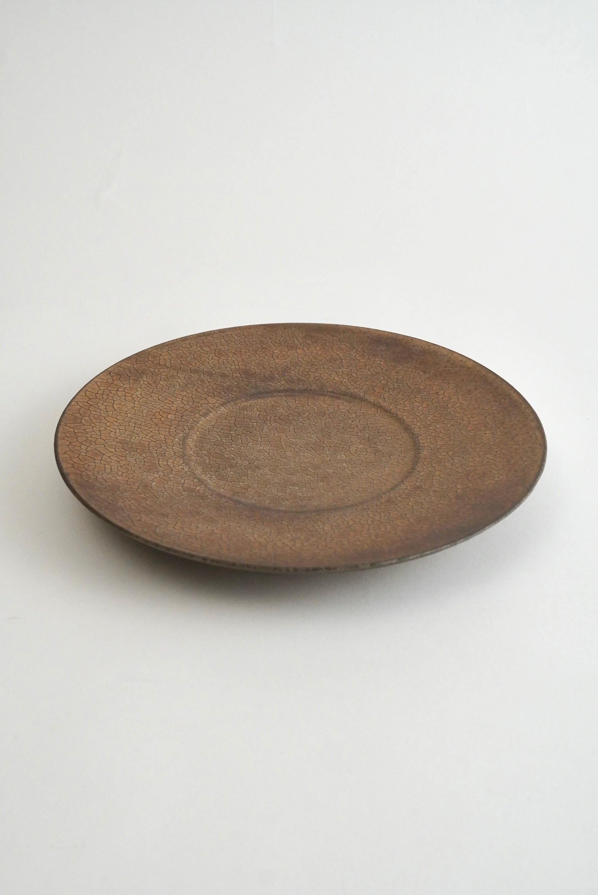A round, shallow ceramic plate or tray with a textured, matte brown glaze, photographed against a clean white background.