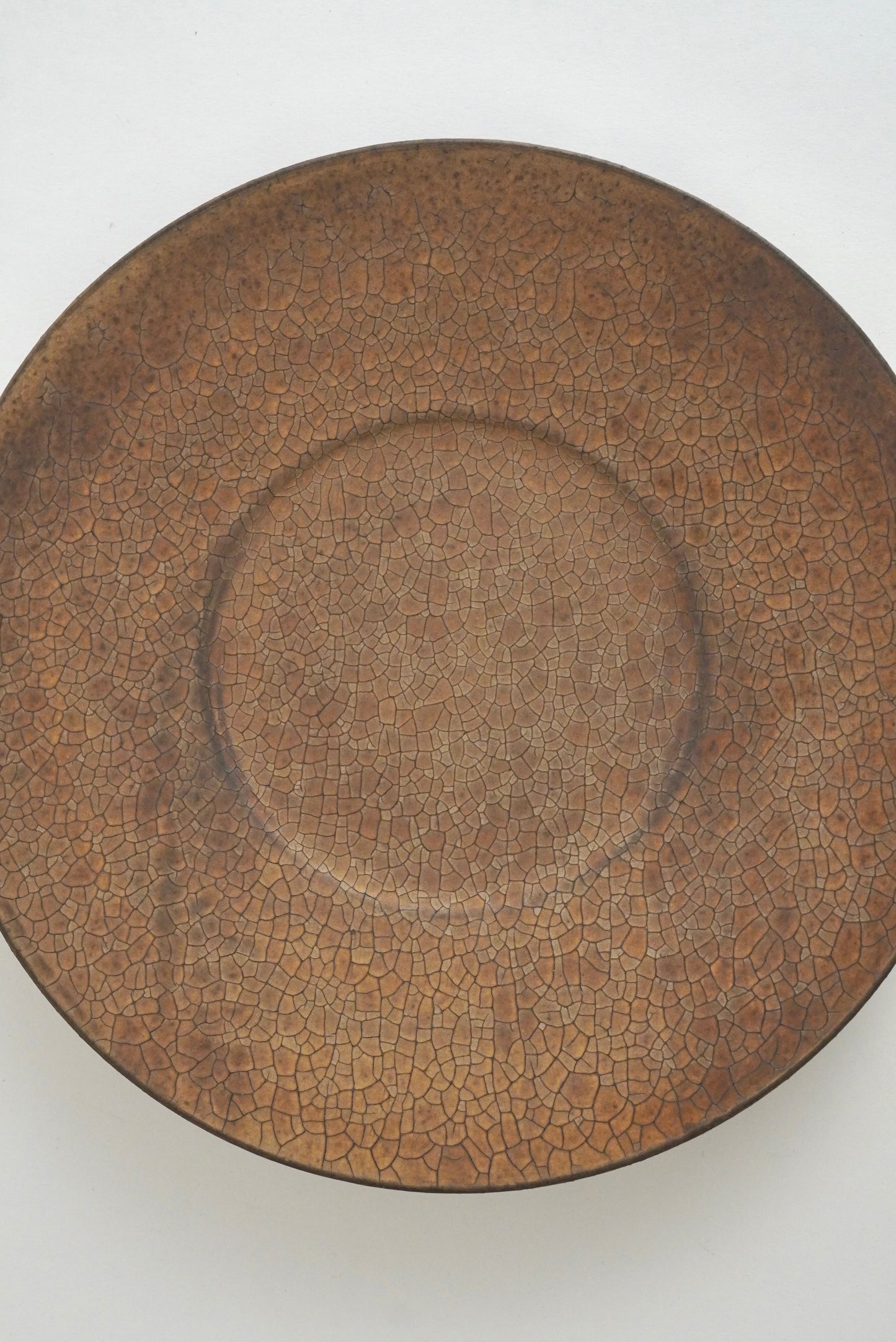 A round ceramic plate with a brown crackle glaze, photographed from directly above on a plain white background.