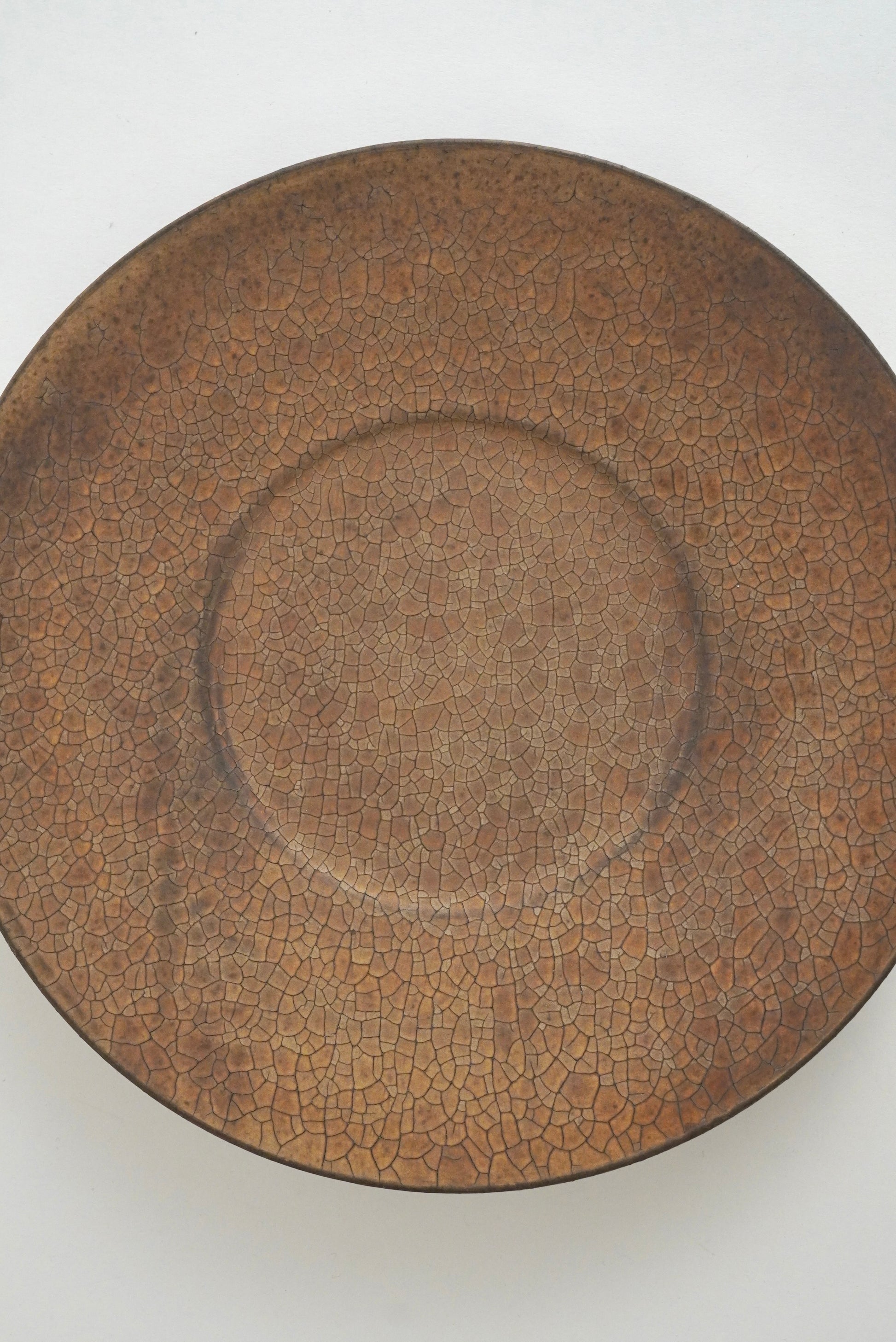 A round ceramic plate with a brown crackle glaze, photographed from directly above on a plain white background.