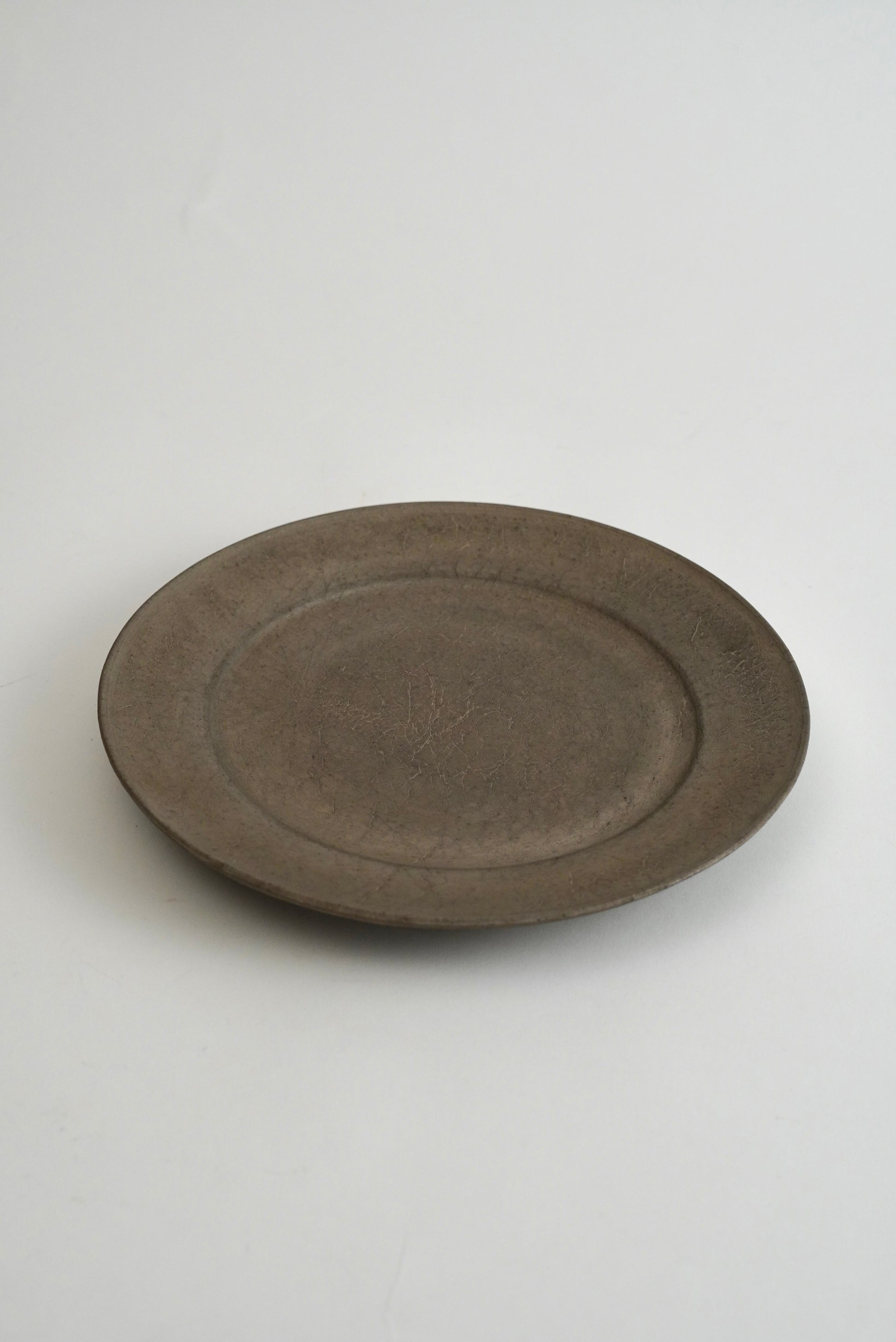 A round, shallow ceramic plate with a matte, textured finish in a dark gray-brown color, photographed on a clean white background.