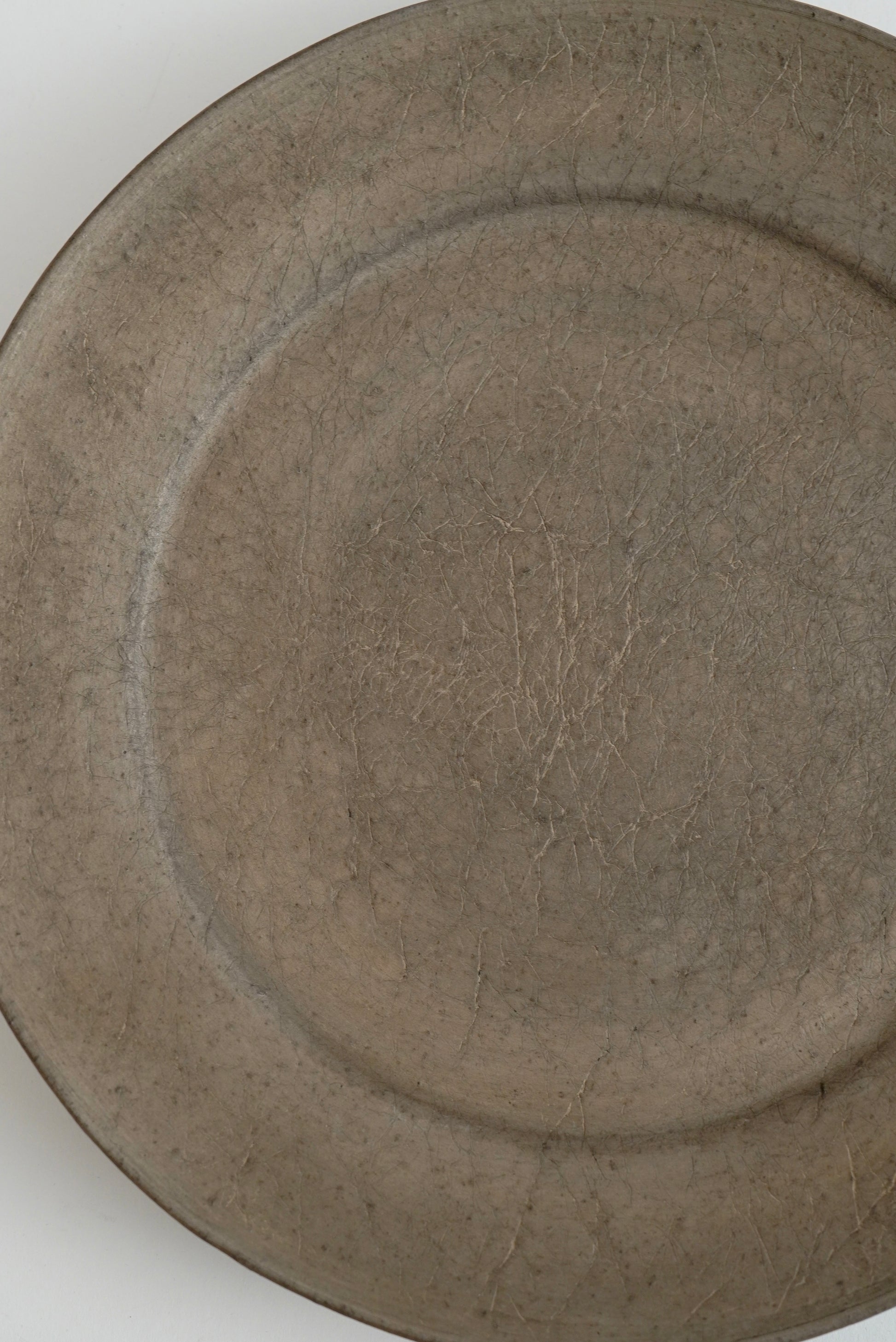 A close-up of a round ceramic plate with a textured, matte finish in a warm gray-brown glaze.