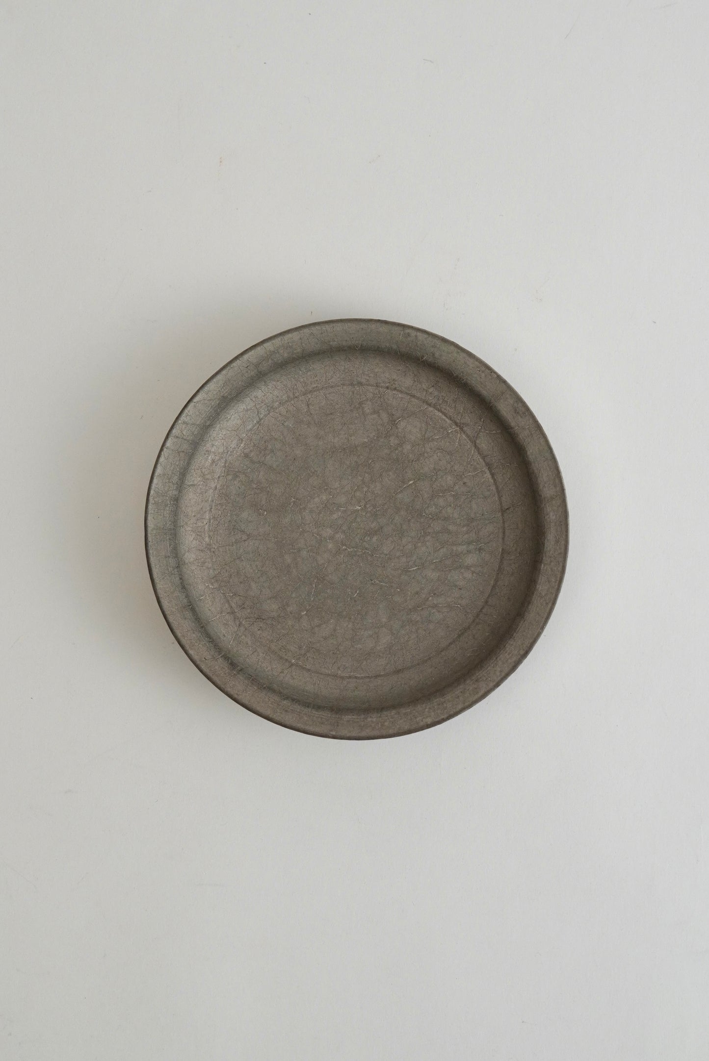 A round, shallow gray ceramic plate or dish with a textured matte finish, photographed from directly above on a clean white background.