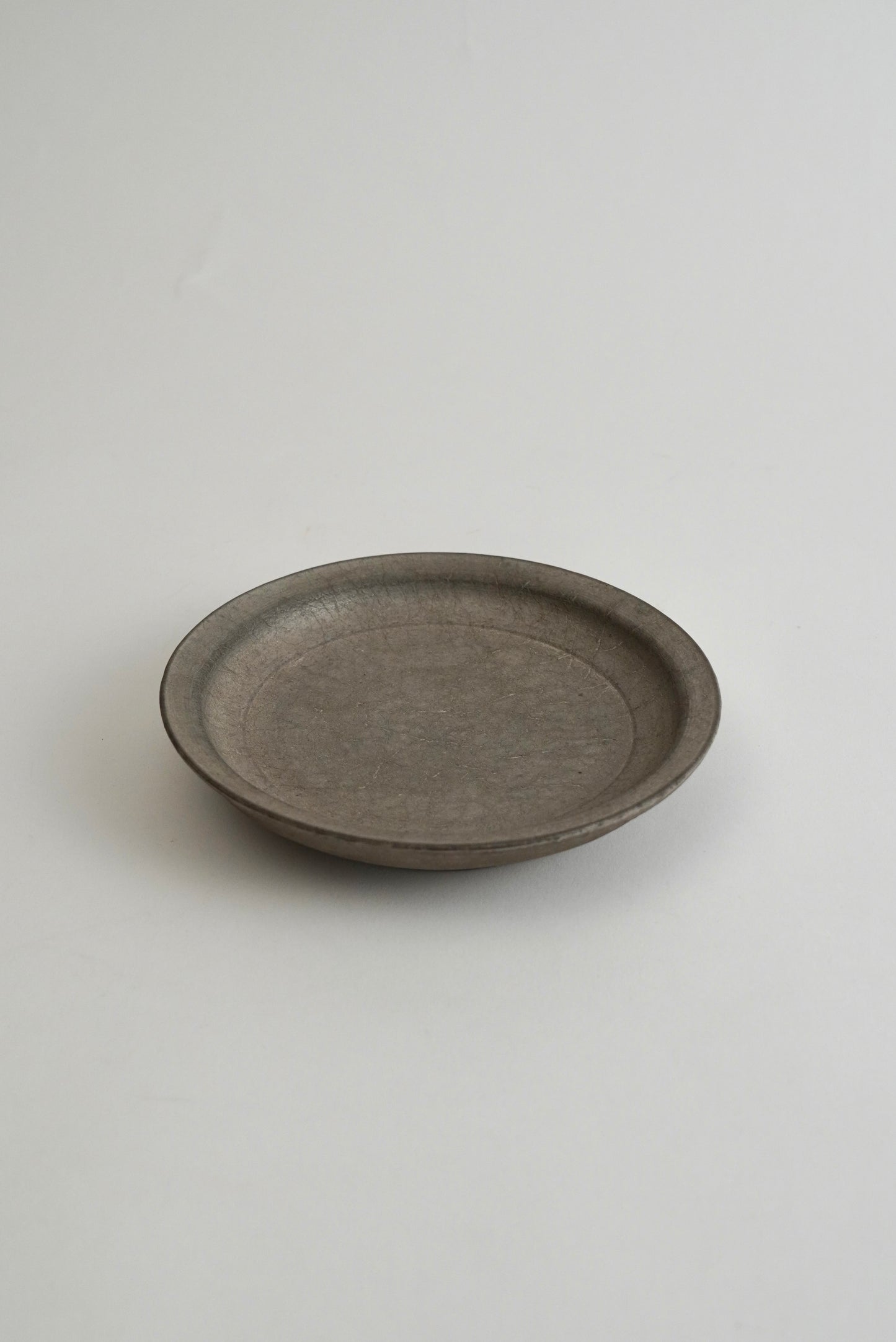 A round, shallow gray ceramic plate with a matte, textured finish, photographed against a neutral light gray background.