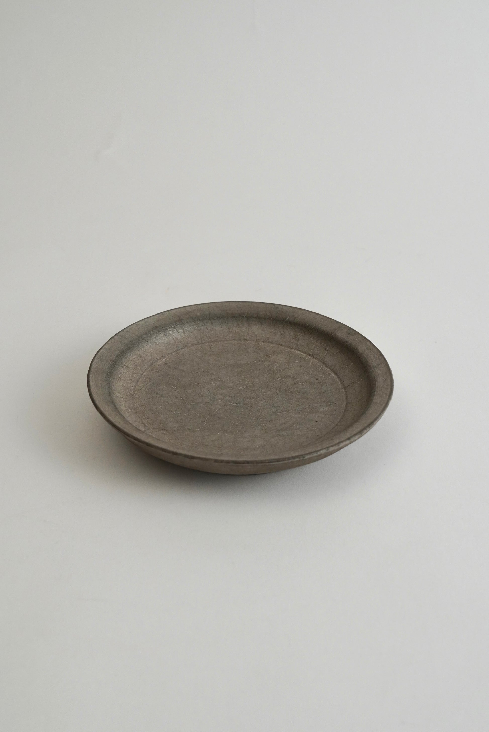 A round, shallow gray ceramic plate with a matte, textured finish, photographed against a neutral light gray background.