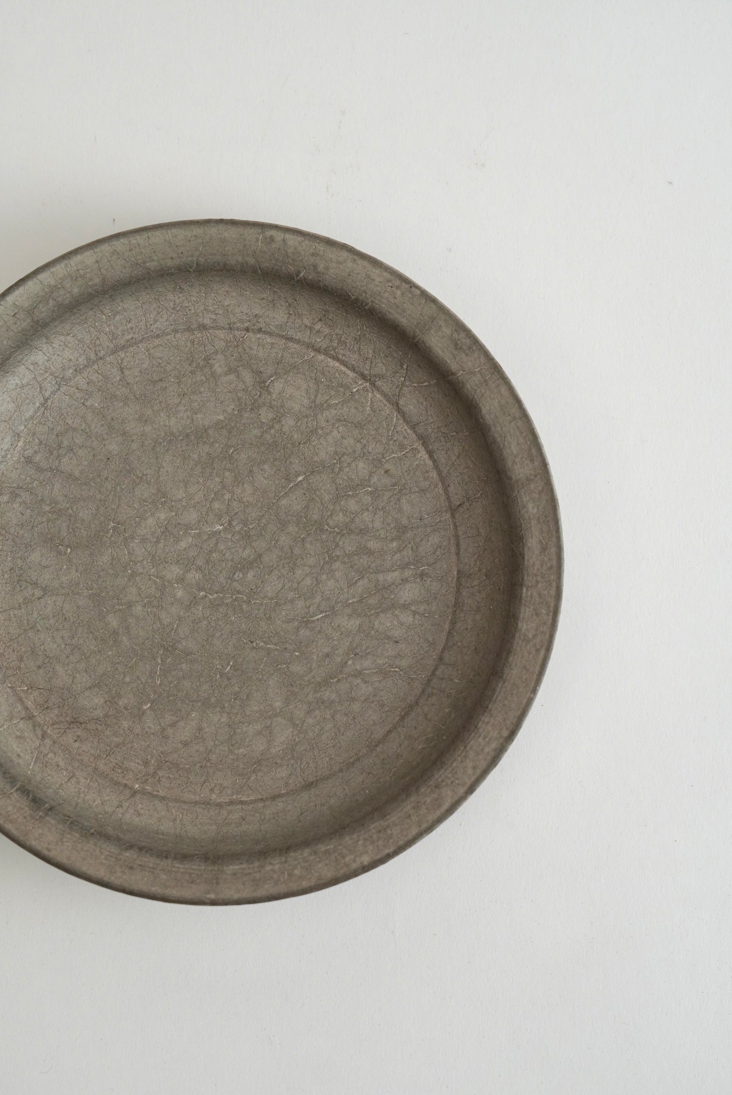 A round, shallow gray ceramic dish with a textured, crackled glaze, photographed from a top-down perspective on a plain white background.