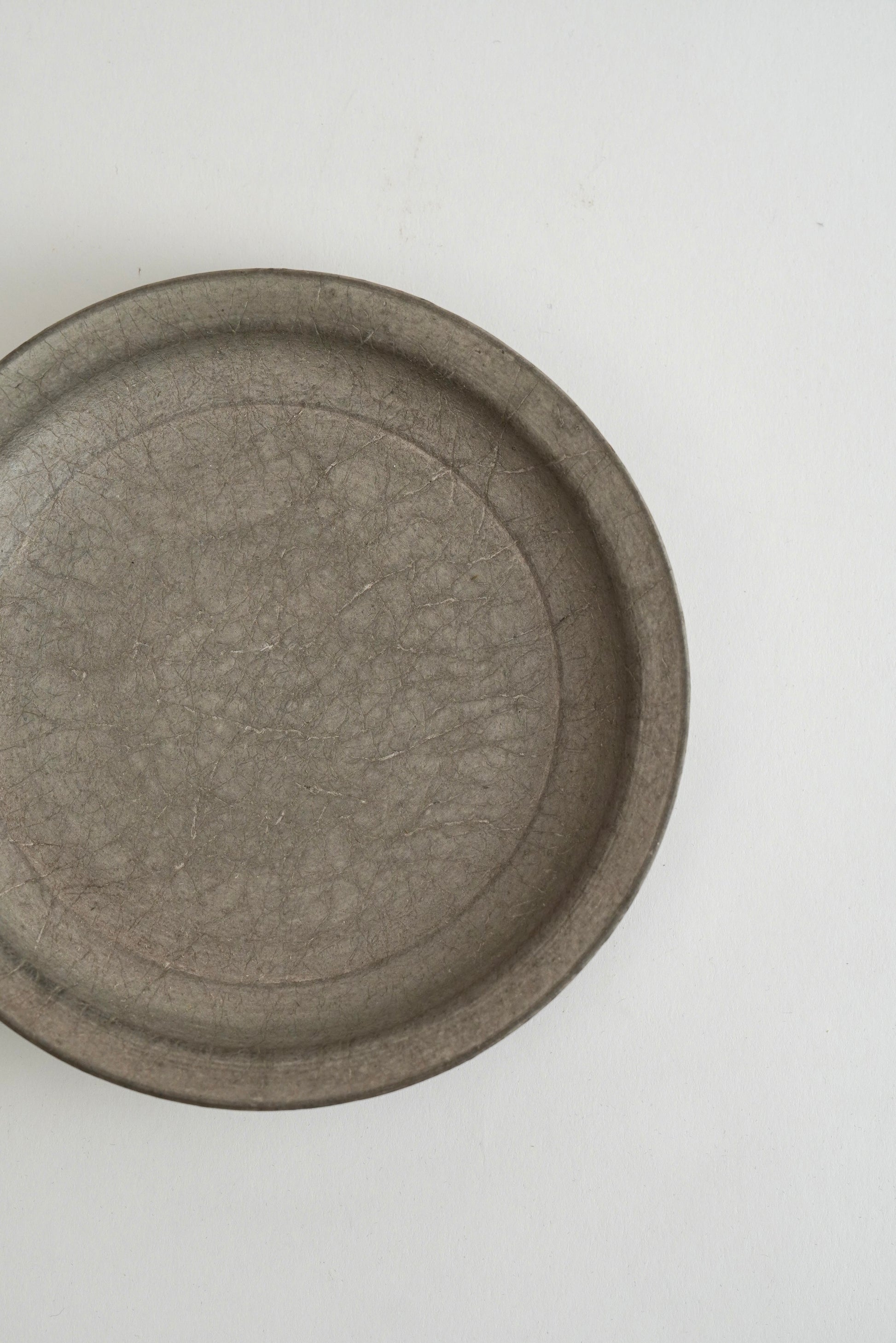 A round, shallow gray ceramic dish with a textured, crackled glaze, photographed from a top-down perspective on a plain white background.