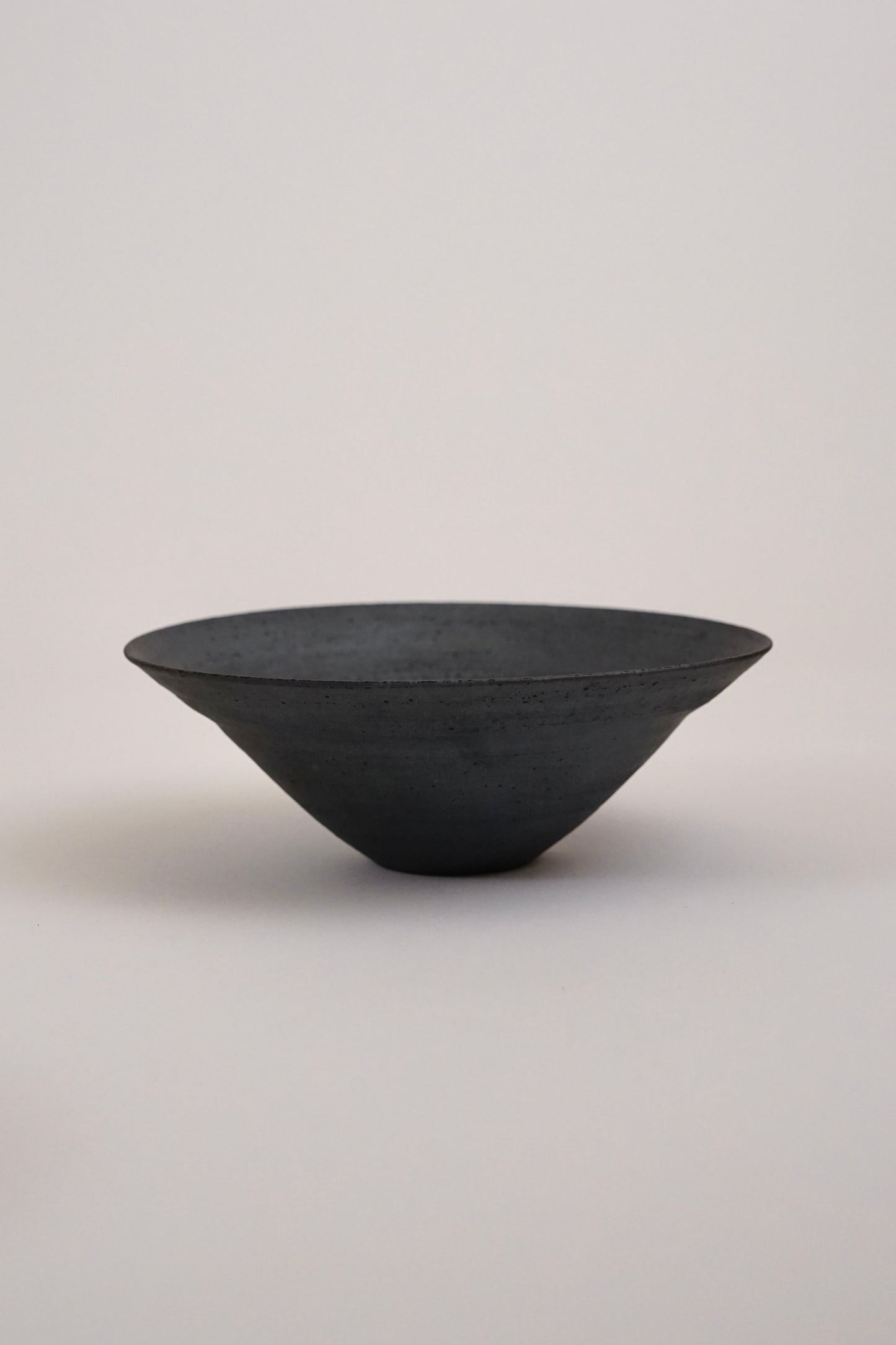 A dark charcoal gray ceramic bowl with a textured matte finish, photographed against a neutral light gray background.