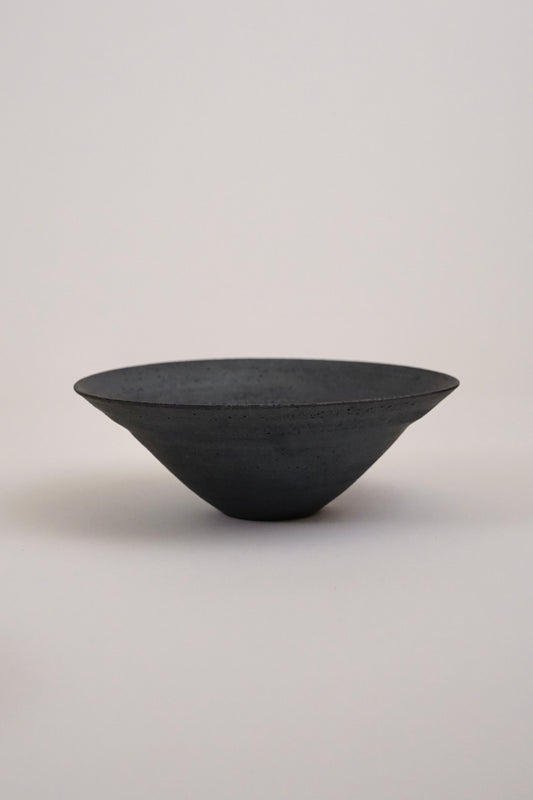 A dark charcoal gray ceramic bowl with a textured matte finish, photographed against a neutral light gray background.