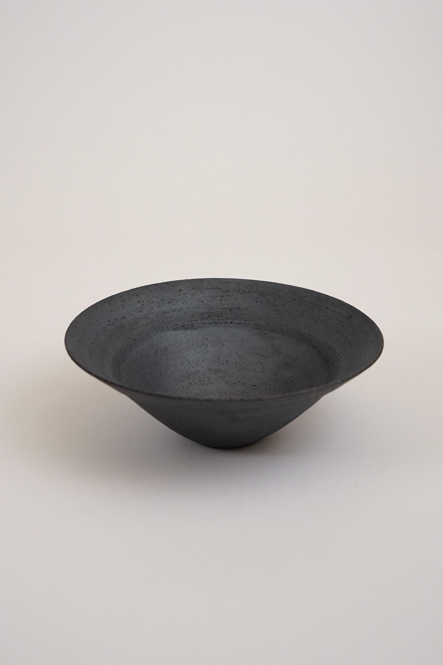 A dark charcoal gray ceramic bowl with a textured matte finish, photographed against a neutral light gray background.