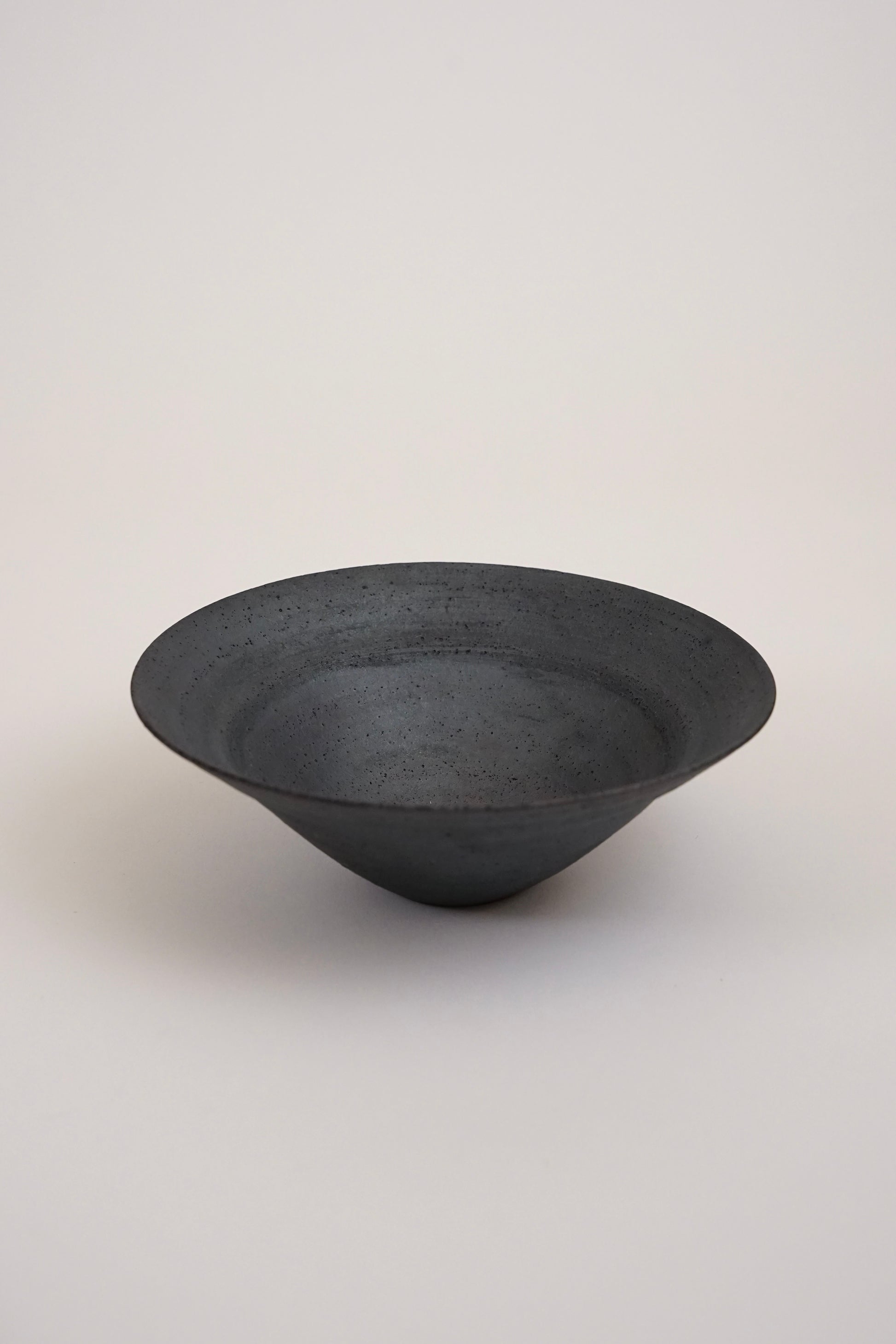 A dark charcoal gray ceramic bowl with a textured matte finish, photographed against a neutral light gray background.