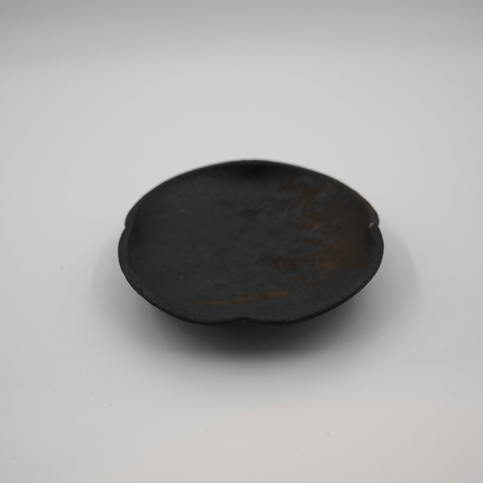Black ceramic plate on a white background. Handmade ceramic  plate by Japanese artist at Gallery tete Hong Kong.