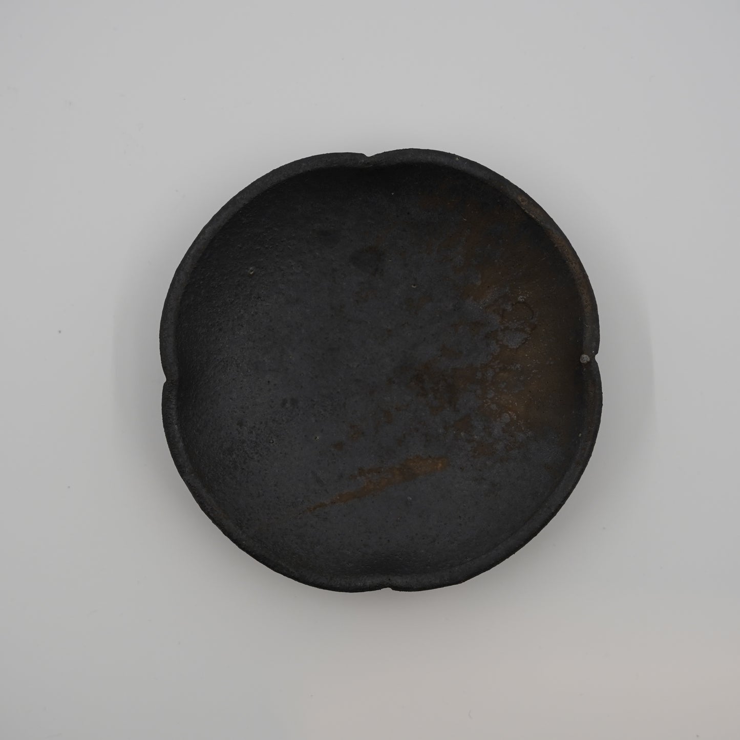 Black ceramic dish on a light gray background. Handmade ceramic  plate by Japanese artist at Gallery tete Hong Kong.