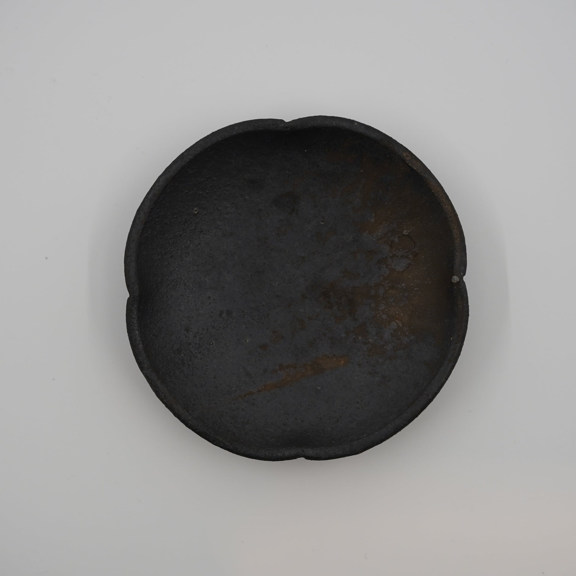 Black ceramic dish on a light gray background. Handmade ceramic  plate by Japanese artist at Gallery tete Hong Kong.