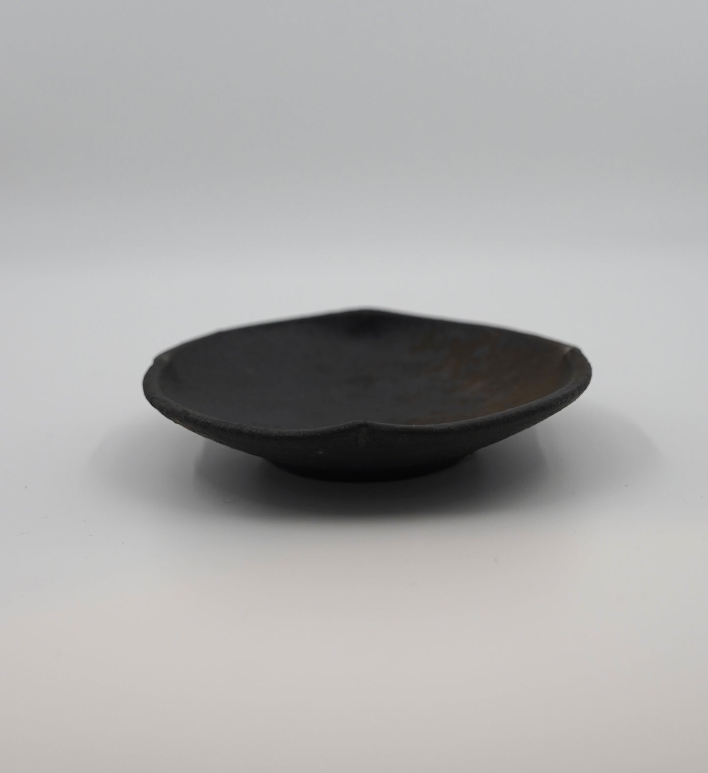 Black ceramic bowl on a gray background. Handmade ceramic  plate by Japanese artist at Gallery tete Hong Kong.