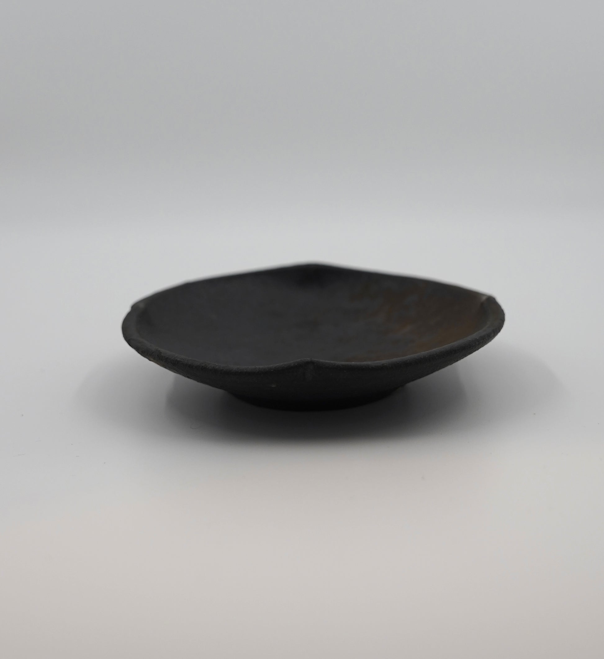 Black ceramic bowl on a gray background. Handmade ceramic  plate by Japanese artist at Gallery tete Hong Kong.