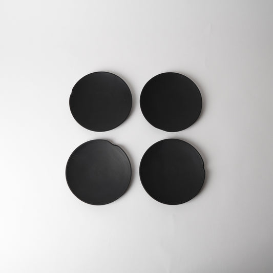Four black round  side plates on a light gray background