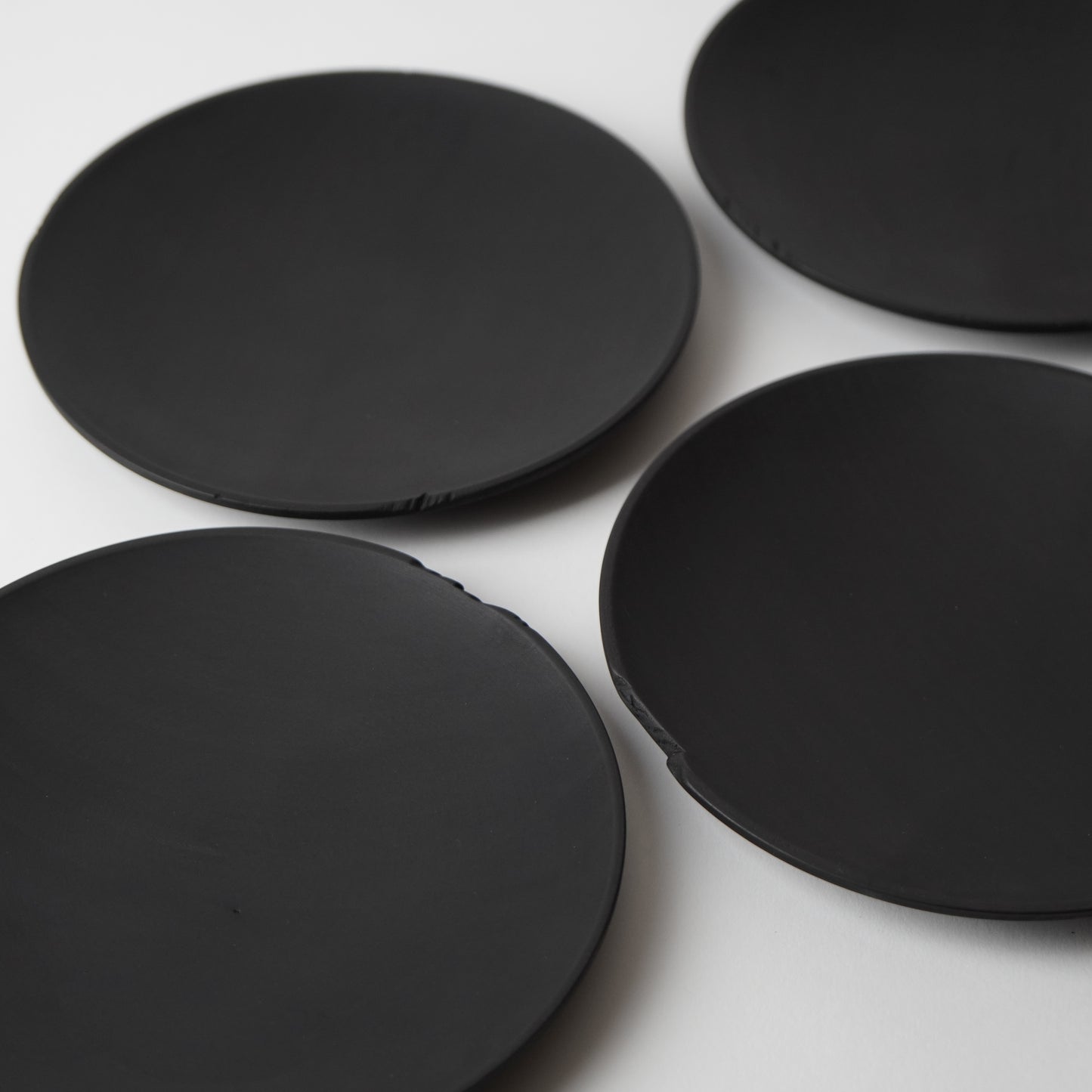 Four black round side plates on a white surface