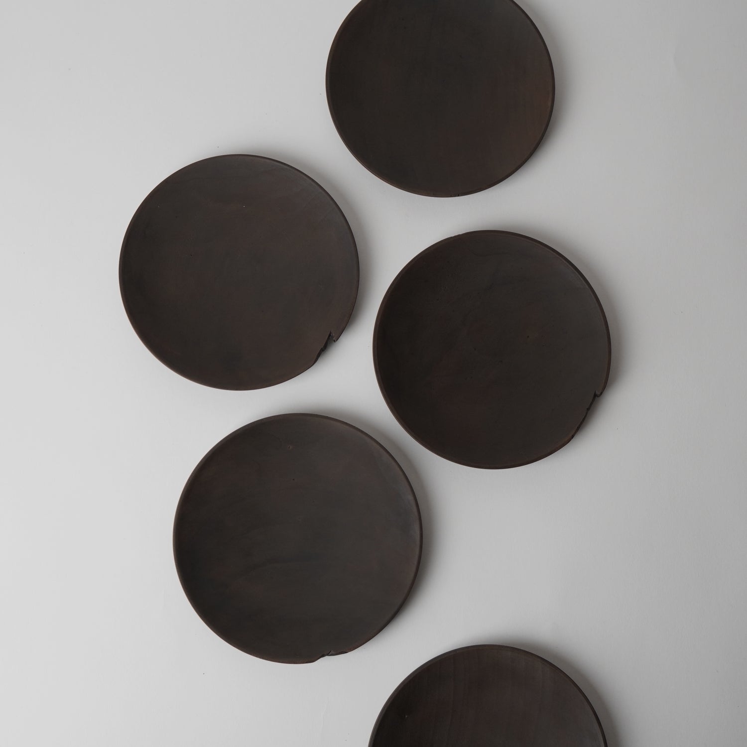 Five dark brown round plates on a light gray background