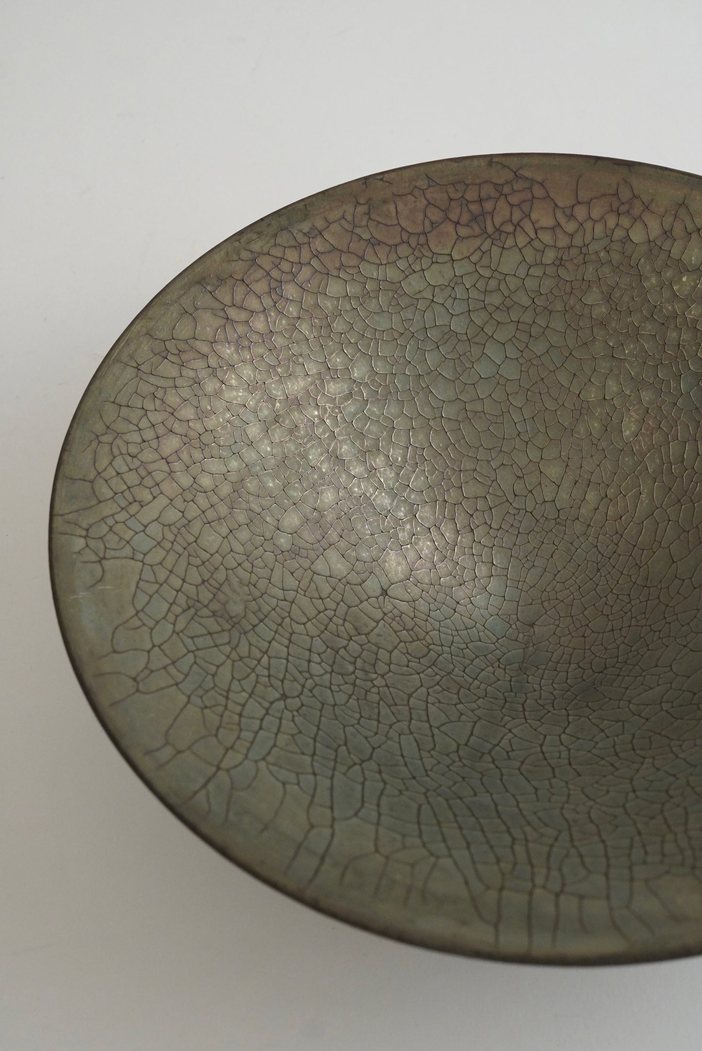 A close-up of a ceramic bowl or dish with a dark gray and brown glaze featuring a prominent crackle pattern, photographed against a plain light background.