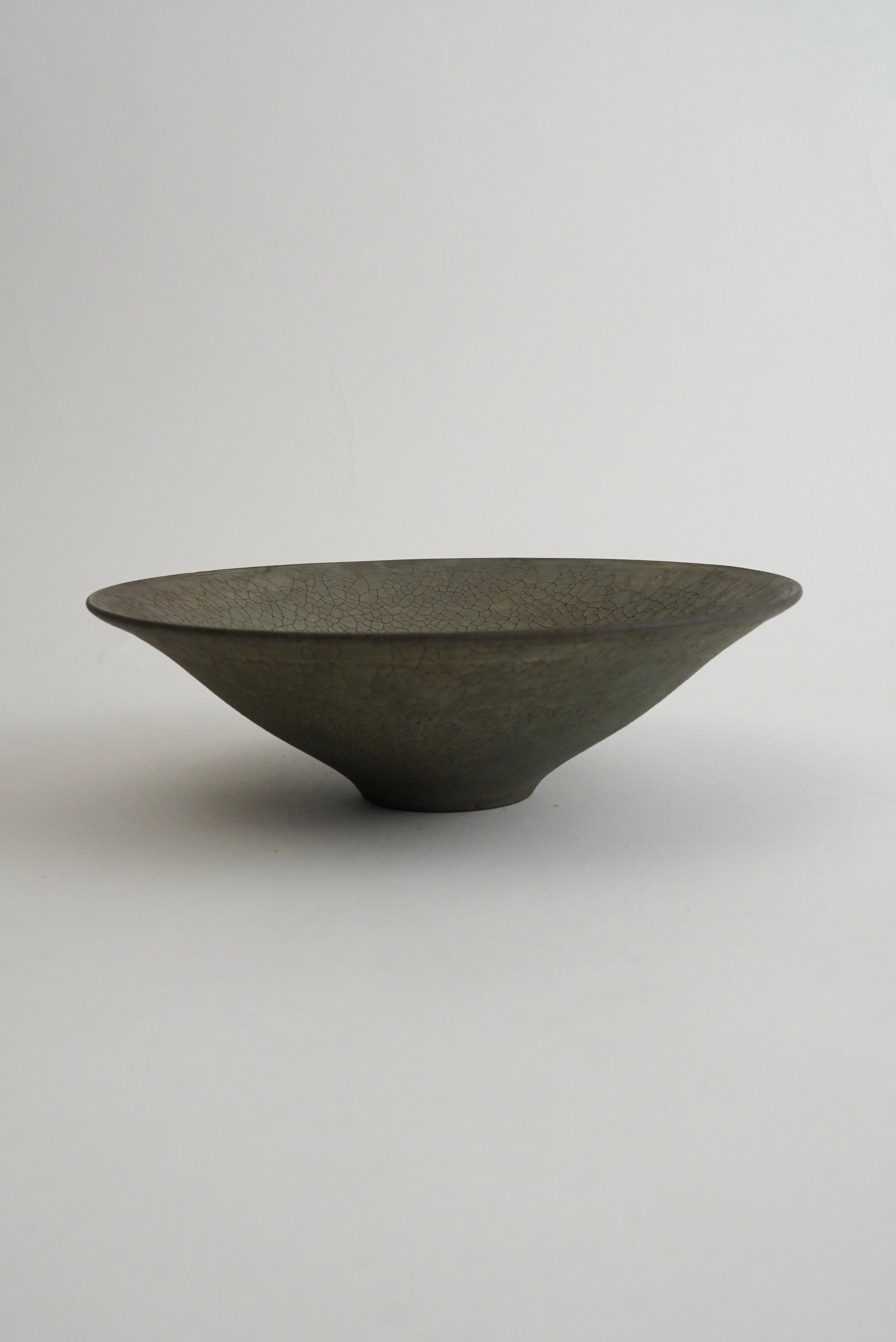 A dark gray, wide-mouthed ceramic bowl with a textured matte finish, photographed against a neutral light gray background.