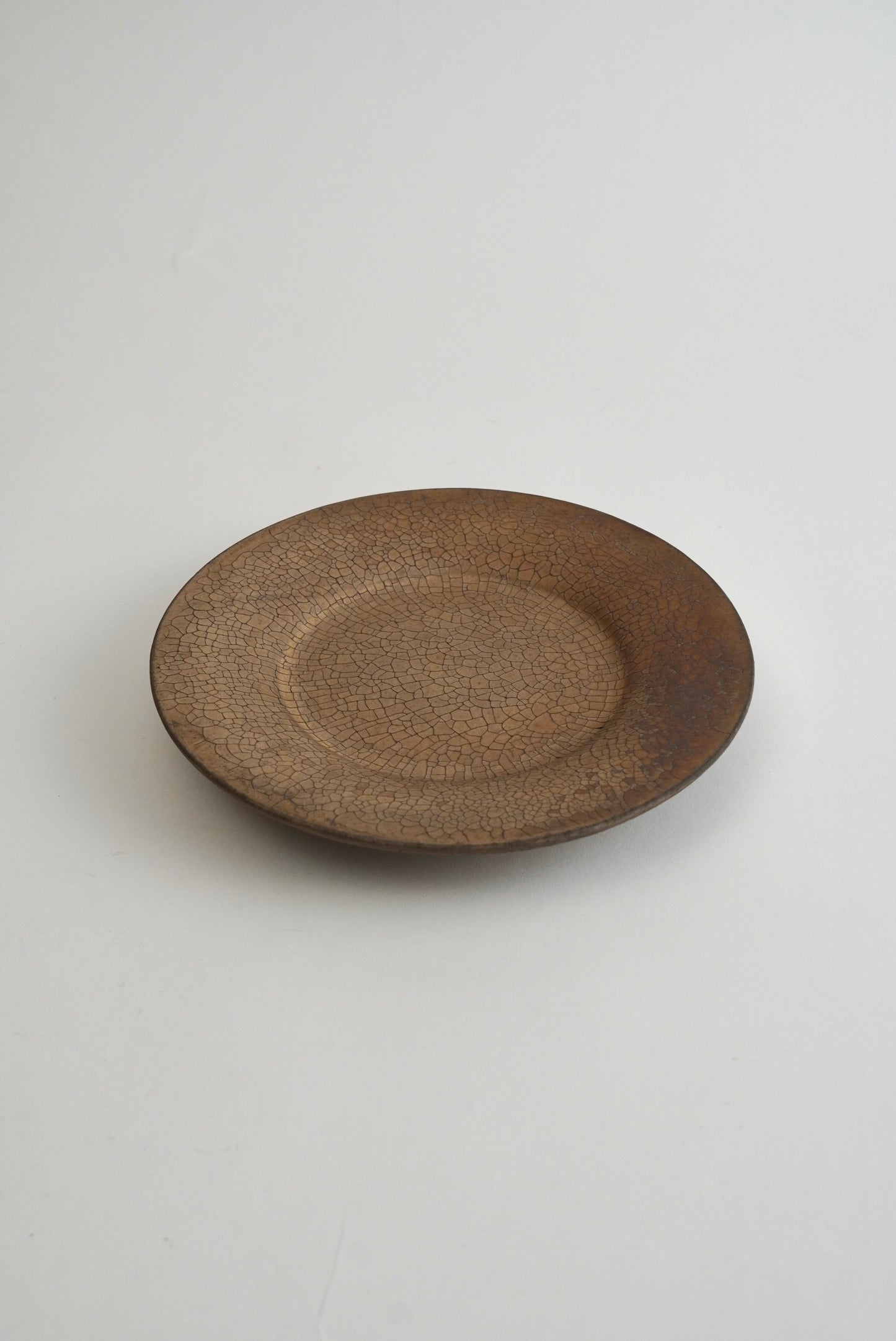 A round ceramic plate with a textured, speckled brown glaze, photographed from a top-down angle on a light gray background.