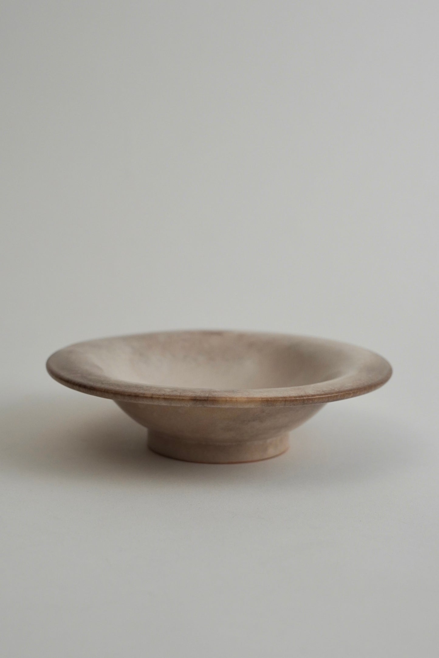 A small, shallow ceramic bowl with a wide rim and a short pedestal base, shown on a plain light gray background.
