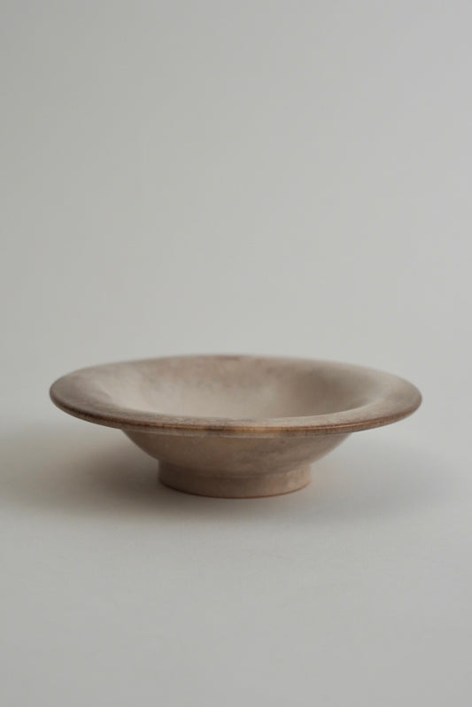 A small, shallow ceramic bowl with a wide rim and a short pedestal base, shown on a plain light gray background.