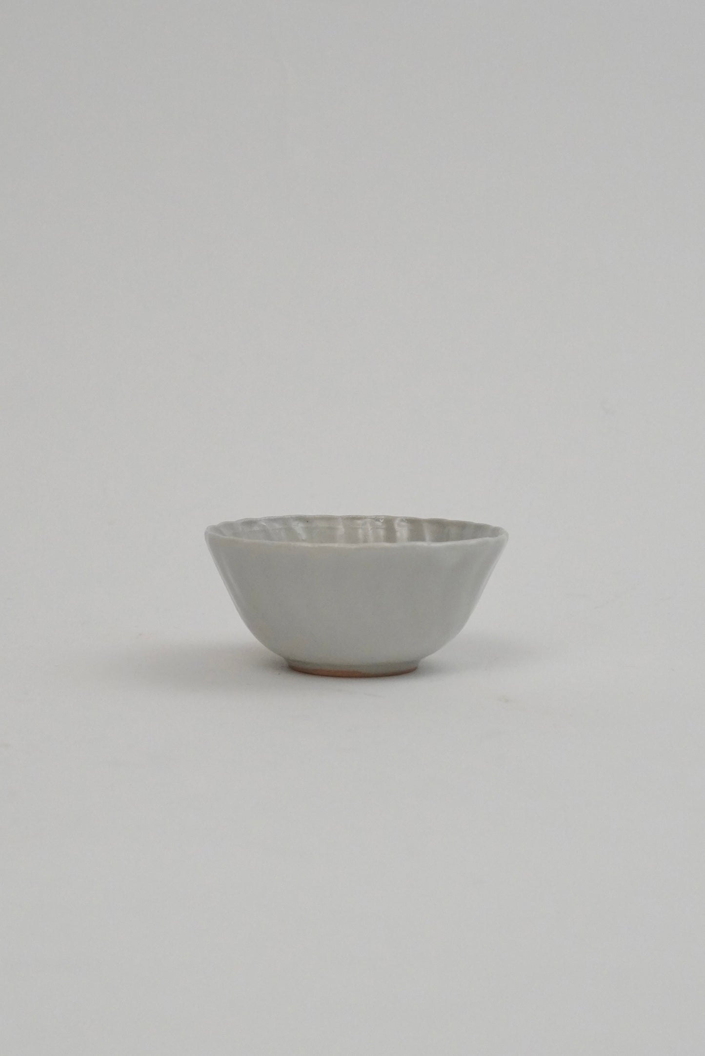 A small ceramic bowl with a textured, ribbed exterior and a smooth, matte off-white interior, set against a plain light gray background.