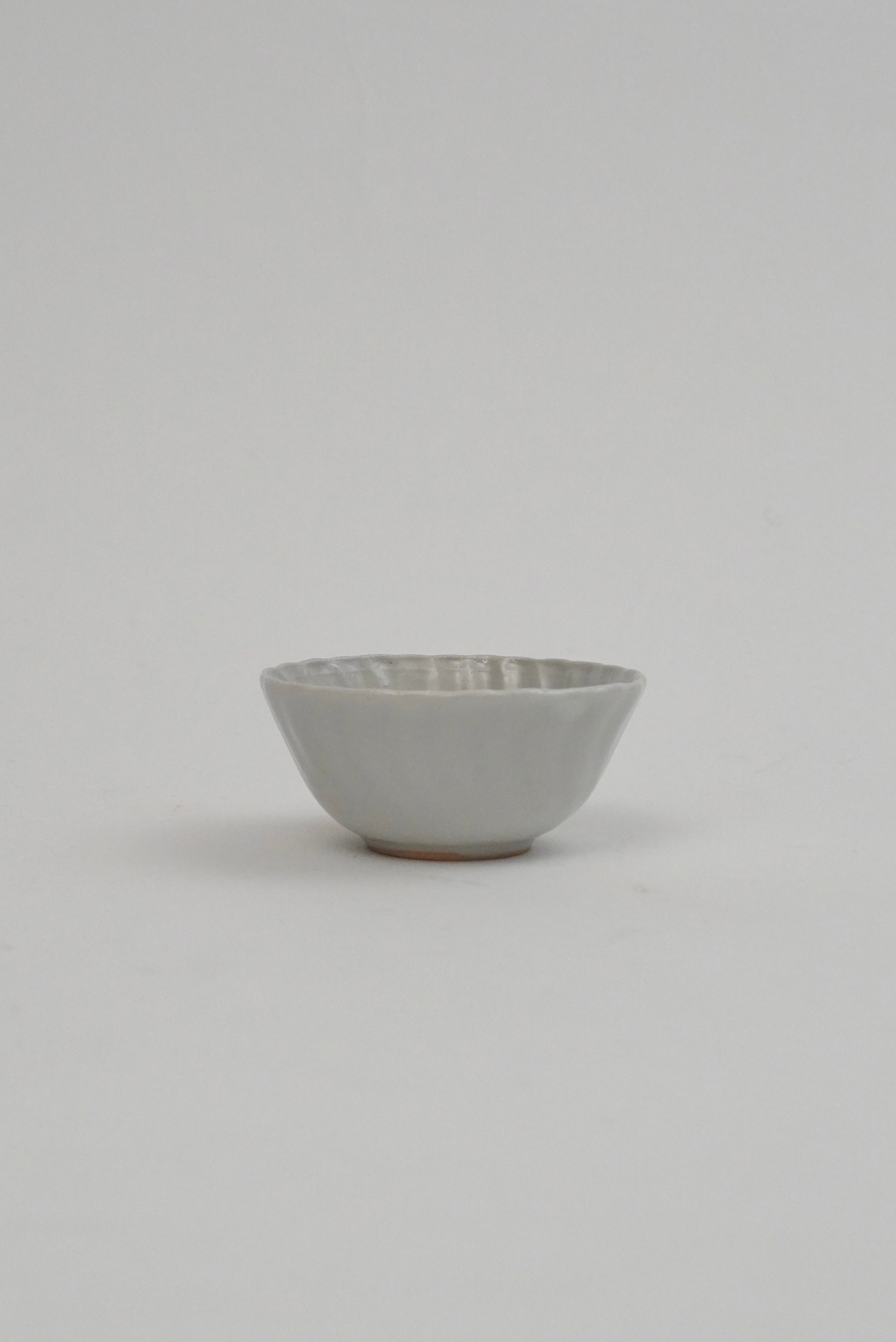 A small ceramic bowl with a textured, ribbed exterior and a smooth, matte off-white interior, set against a plain light gray background.