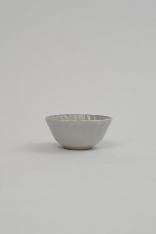 A small ceramic bowl with a textured, ribbed exterior and a smooth, matte off-white interior, set against a plain light gray background.