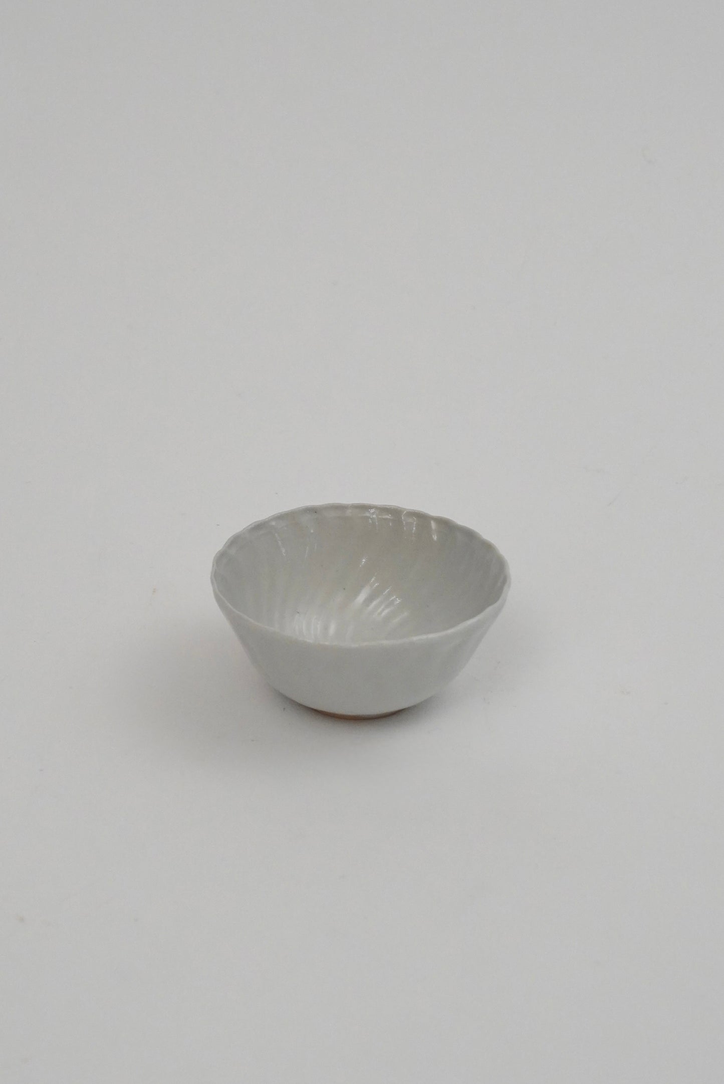 A small white ceramic bowl with a textured, ribbed exterior and a smooth, slightly glossy interior, photographed against a seamless light gray background.