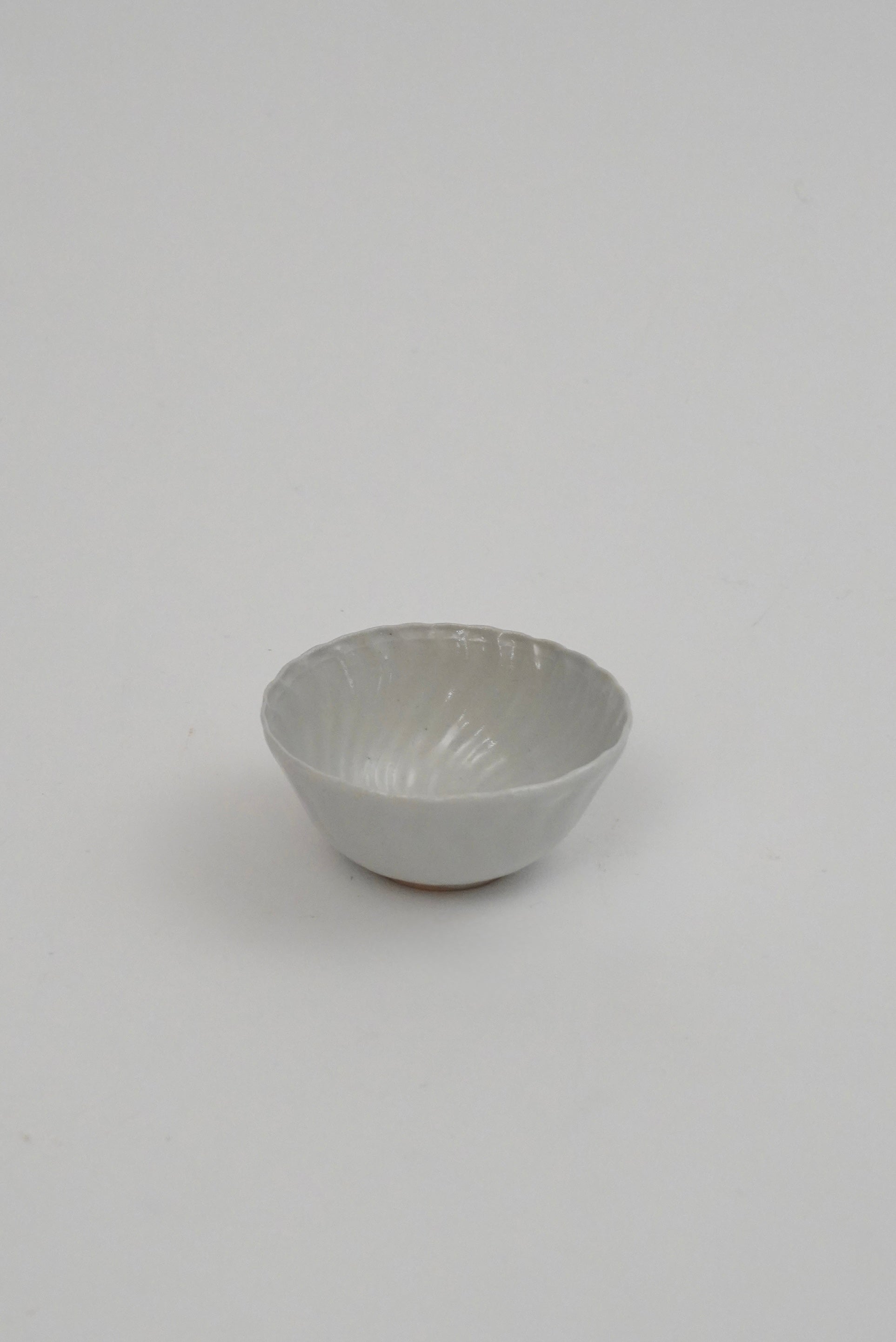 A small white ceramic bowl with a textured, ribbed exterior and a smooth, slightly glossy interior, photographed against a seamless light gray background.