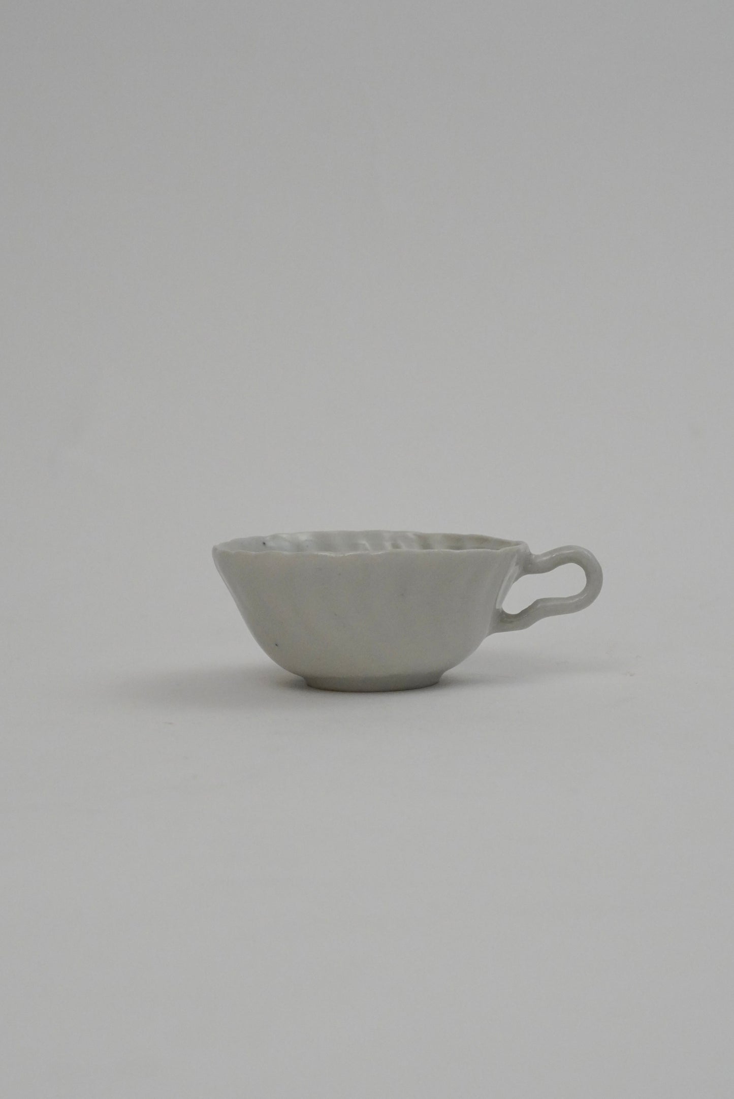 A small light gray ceramic cup with a textured exterior and a loop handle, photographed against a seamless light gray background.