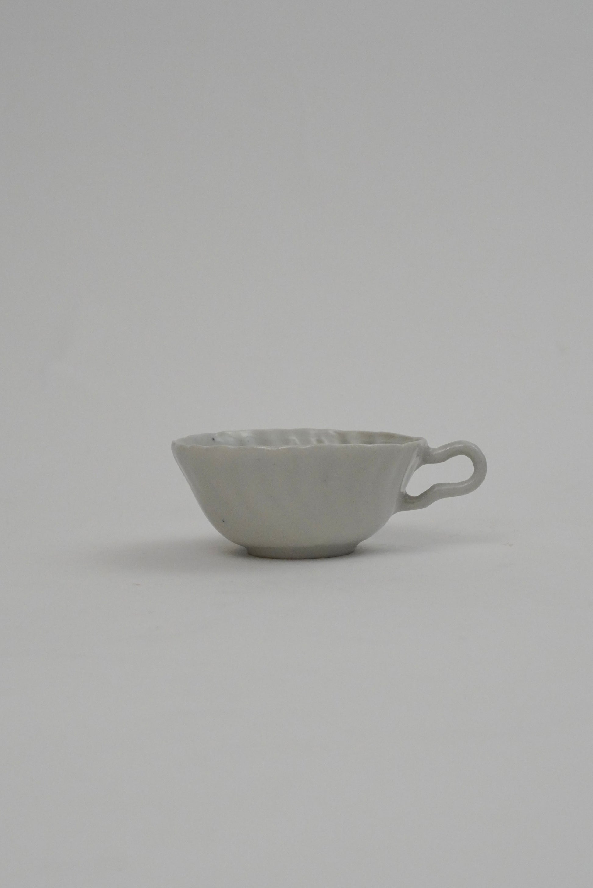 A small light gray ceramic cup with a textured exterior and a loop handle, photographed against a seamless light gray background.