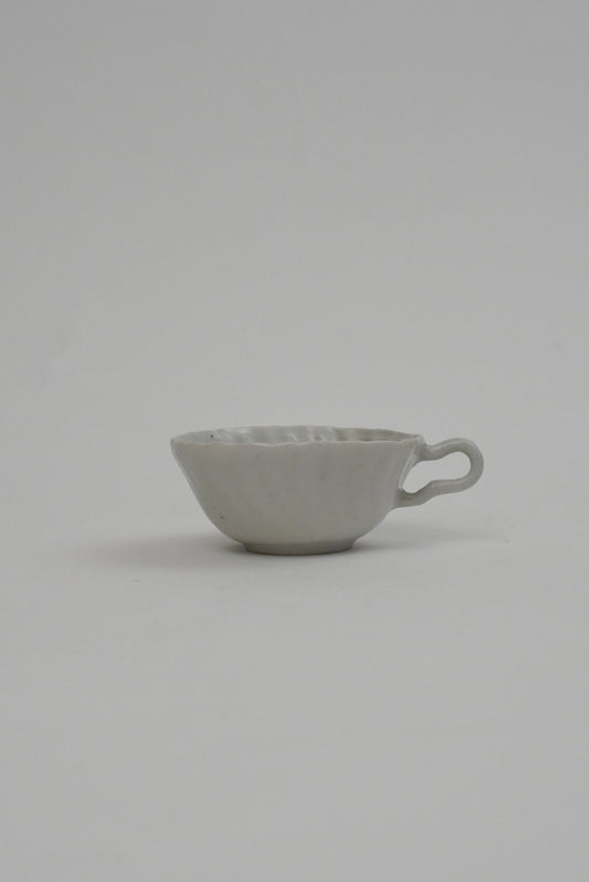 A small light gray ceramic cup with a textured exterior and a loop handle, photographed against a seamless light gray background.