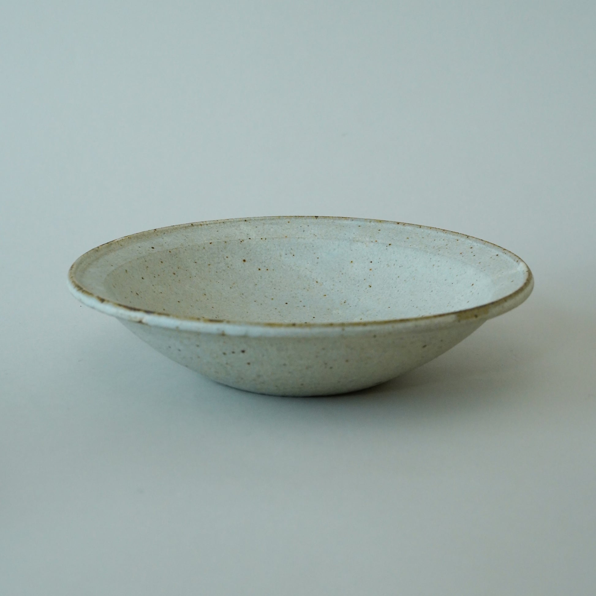 Ceramic bowl with speckled glaze on a light gray background