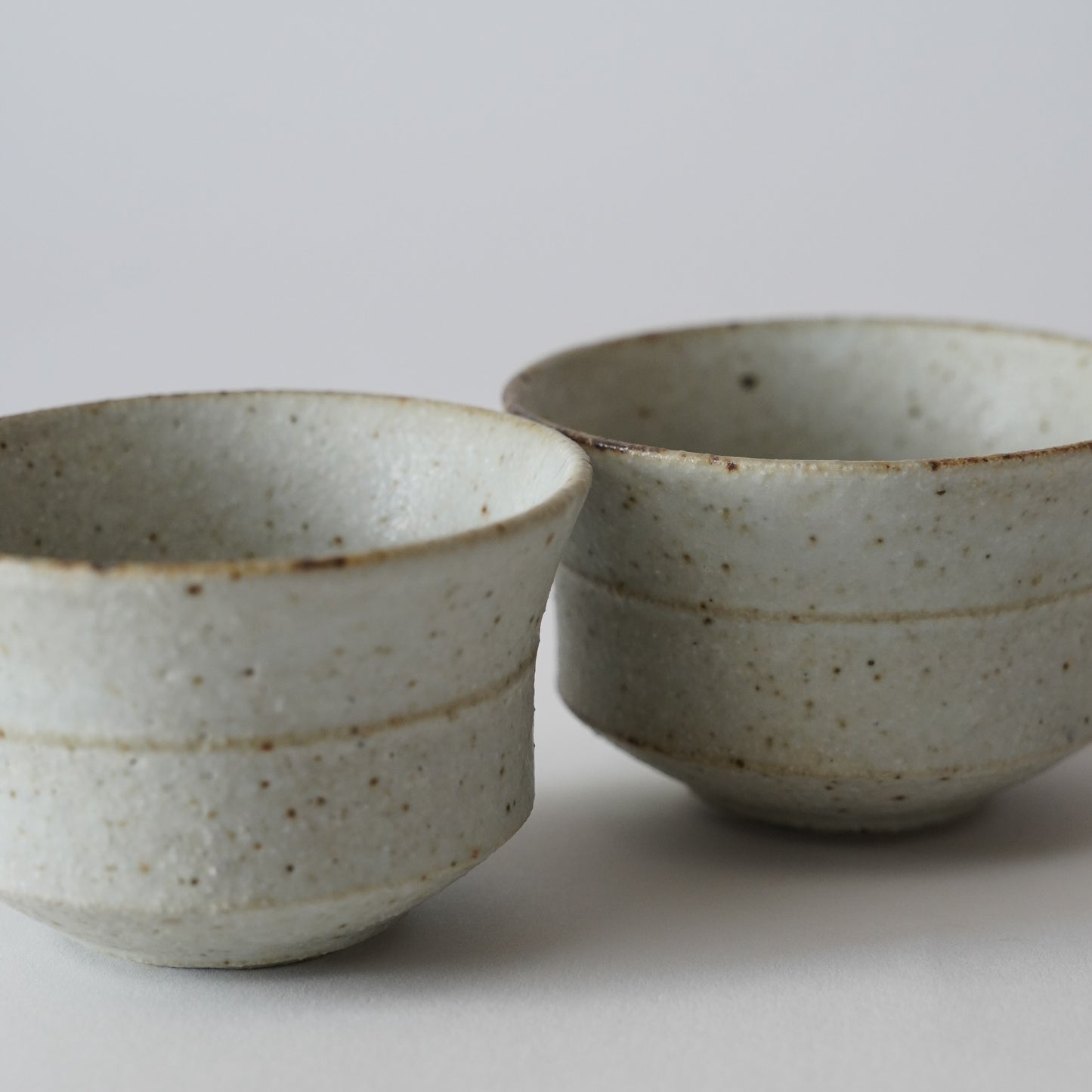 Two ceramic bowls with speckled glaze on a light gray background. Handmade ceramic cup by Japanese artist at Gallery tete Hong Kong.