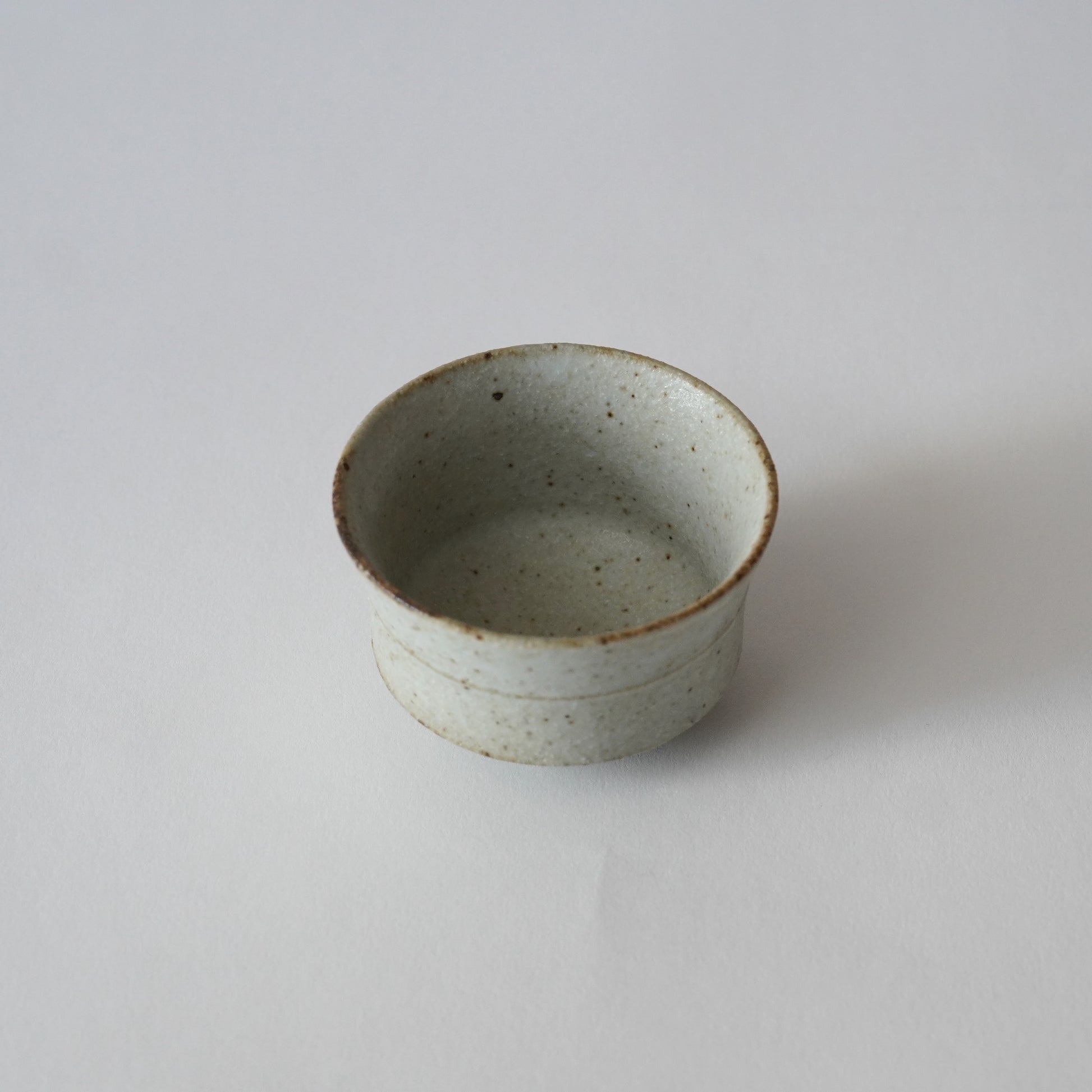 Small ceramic cup with speckled glaze on a white background. Handmade ceramic cup by Japanese artist at Gallery tete Hong Kong.