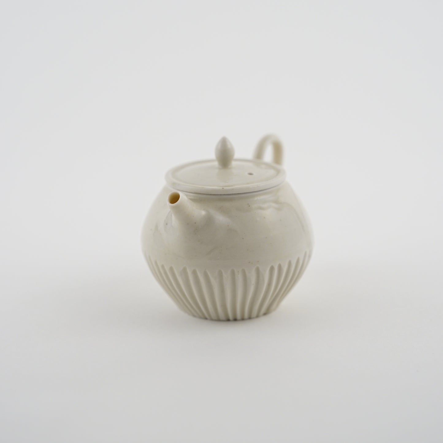White ceramic Chinese teapot made by Japanese Artist with ribbed design on a light gray background.Handmade porcelain chinese teapot by Japanese artist at Gallery tete Hong Kong.