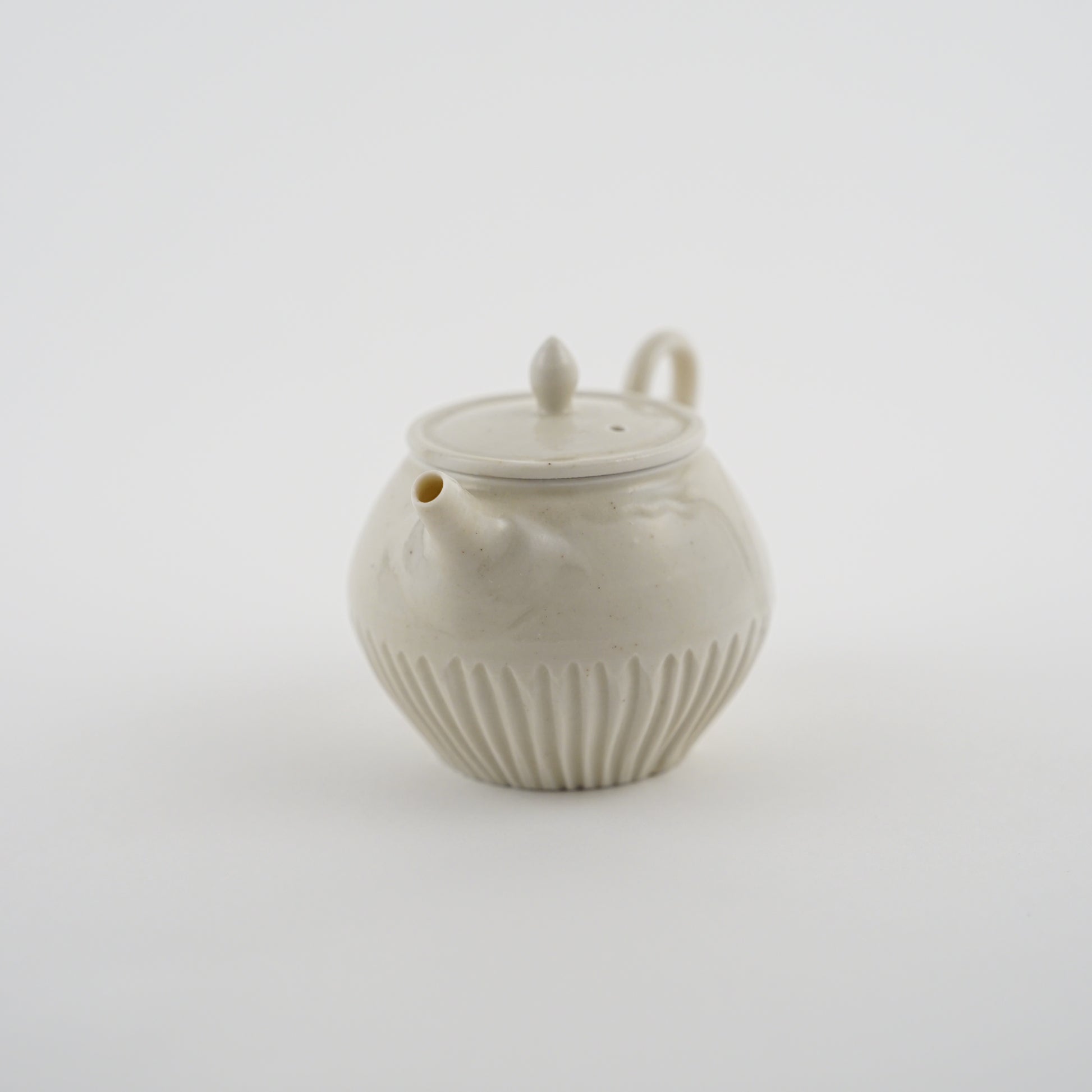 White ceramic Chinese teapot made by Japanese Artist with ribbed design on a light gray background.Handmade porcelain chinese teapot by Japanese artist at Gallery tete Hong Kong.