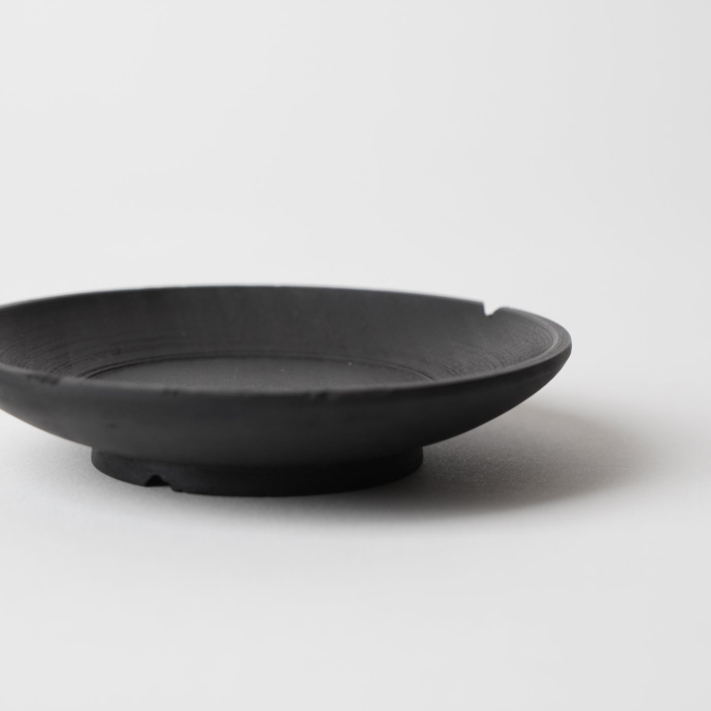 Black wooden saucer on a light gray background. Handmade wooden saucer by Japanese artist at Gallery tete Hong Kong.