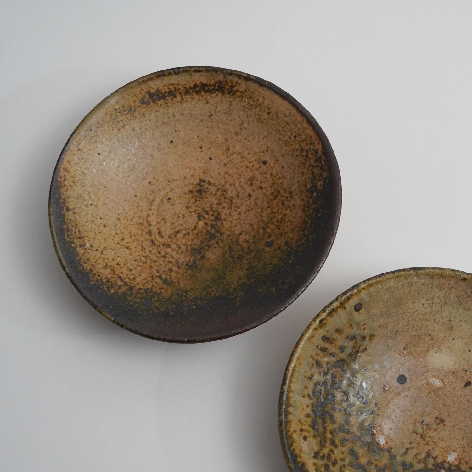 Two ceramic bowls with brown and black speckled glaze on a light gray background