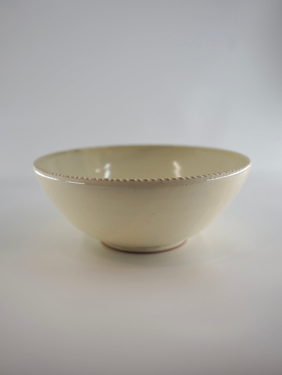 A small cream-colored ceramic bowl with a subtle textured rim, photographed against a neutral light gray background.